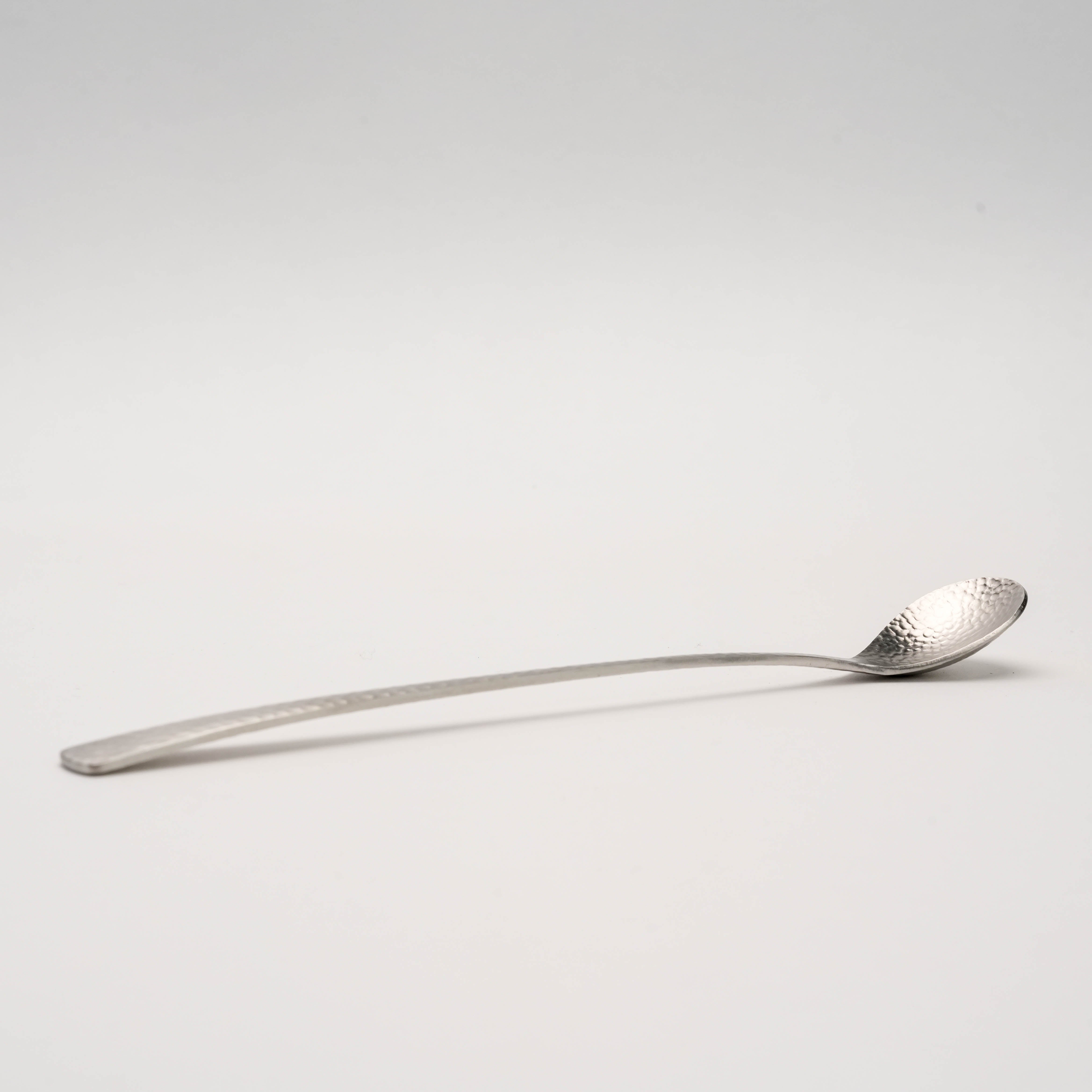 Side view of Nagomi hammered stainless steel drink stirrer, showcasing its slim, curved design for precise cocktail mixing.