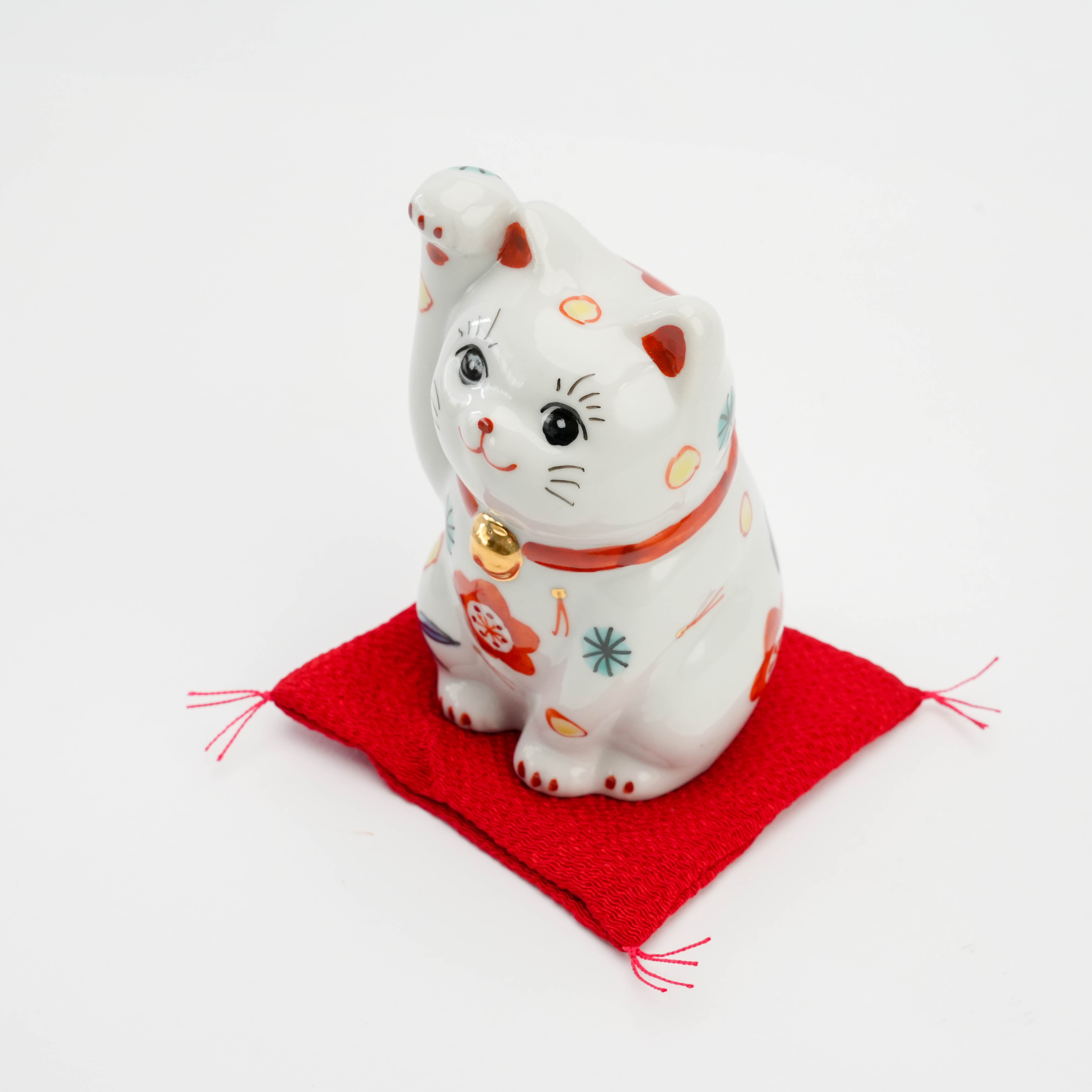 Angled top view of Kutani Ware Cat Figurine on red cushion, showcasing intricate hand-painted Sho Chiku Bai patterns for good fortune.