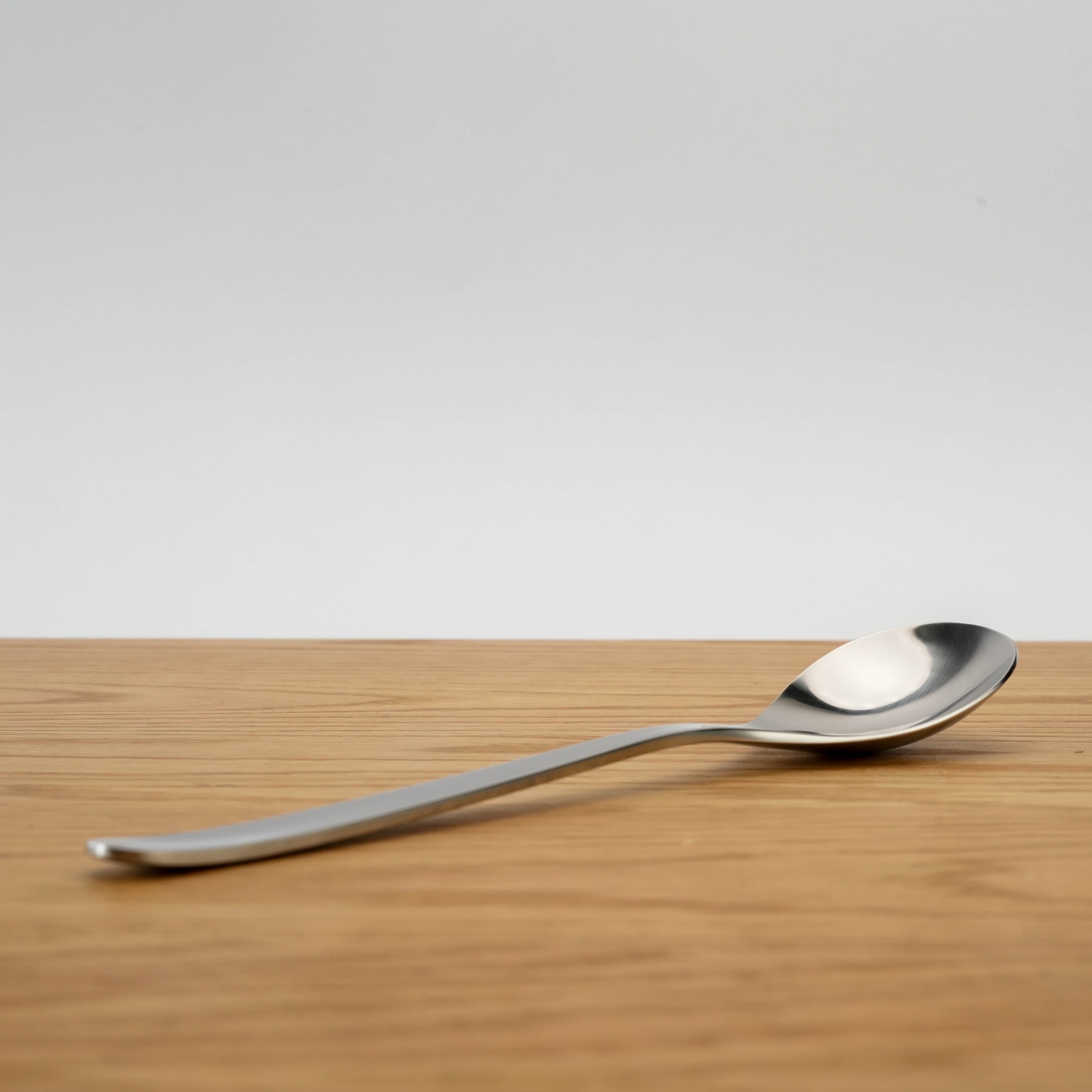 Side view of Sori Yanagi Dinner Spoon highlighting its sleek stainless steel curve and balanced design for comfortable grip.