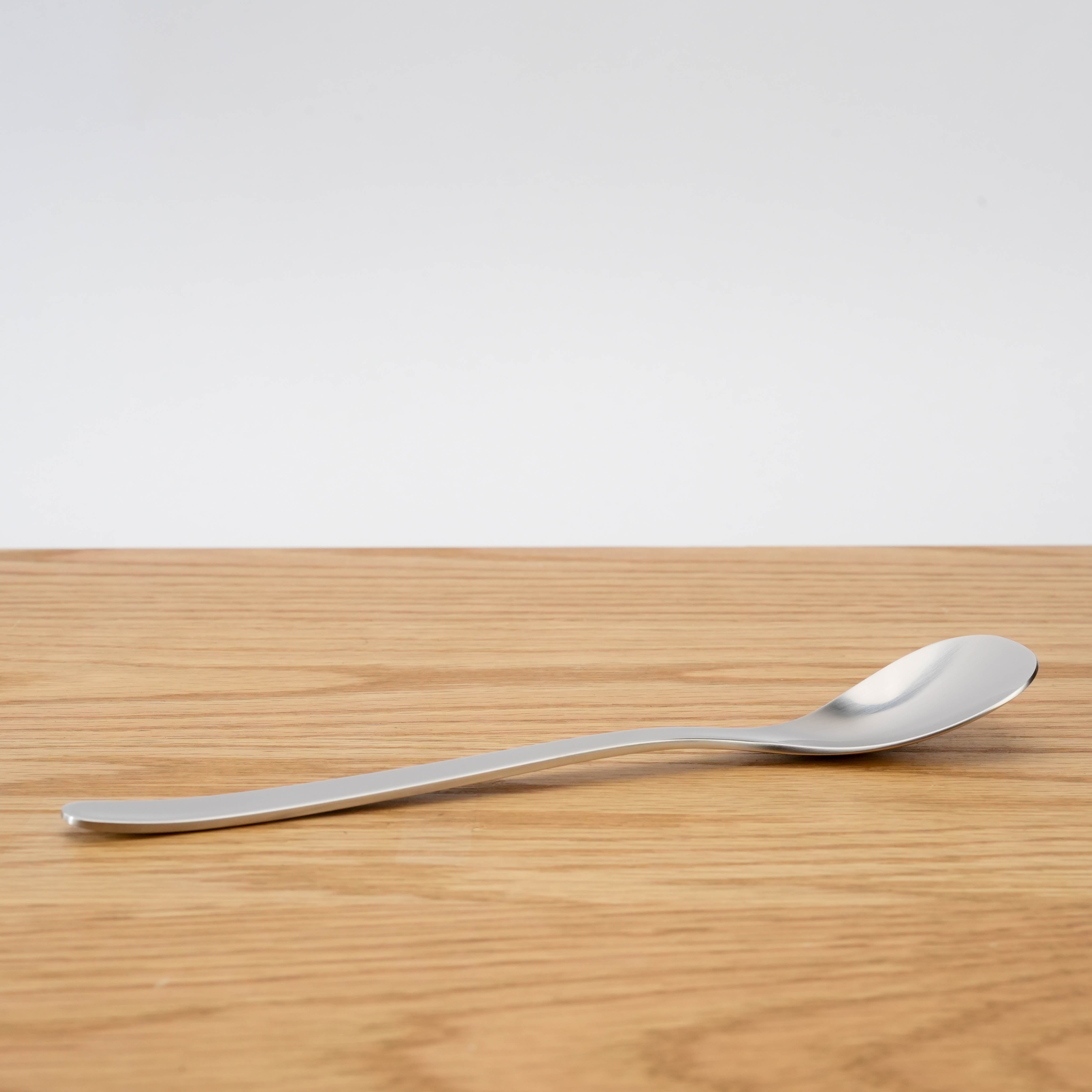 Side view of Sori Yanagi stainless steel curry spoon showing curved handle and seamless steel form for modern kitchen utility.