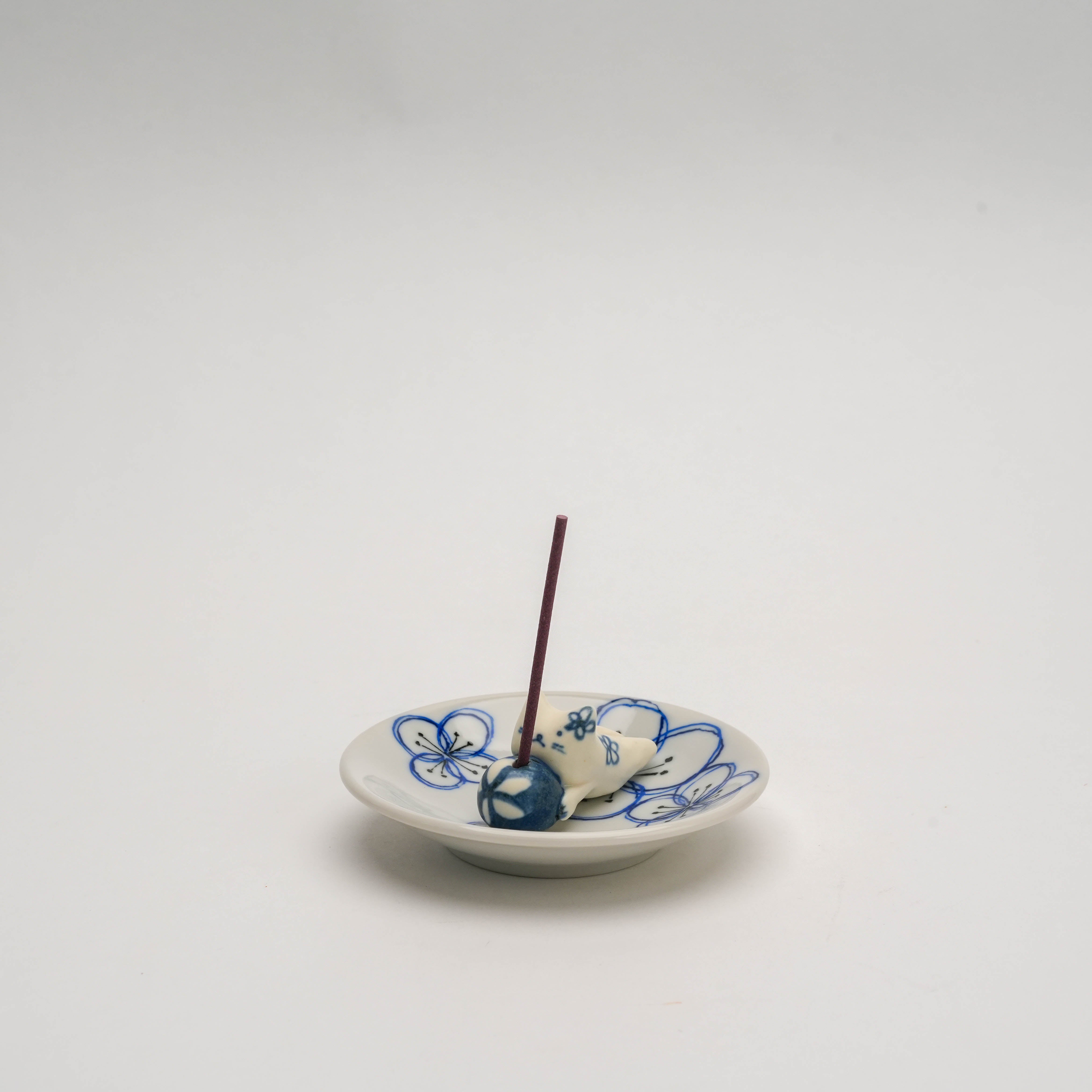 Dyed Flower Cat Incense Holder with Japanese ceramic cat figure and floral motifs, holding a lit incense stick on a decorative dish.
