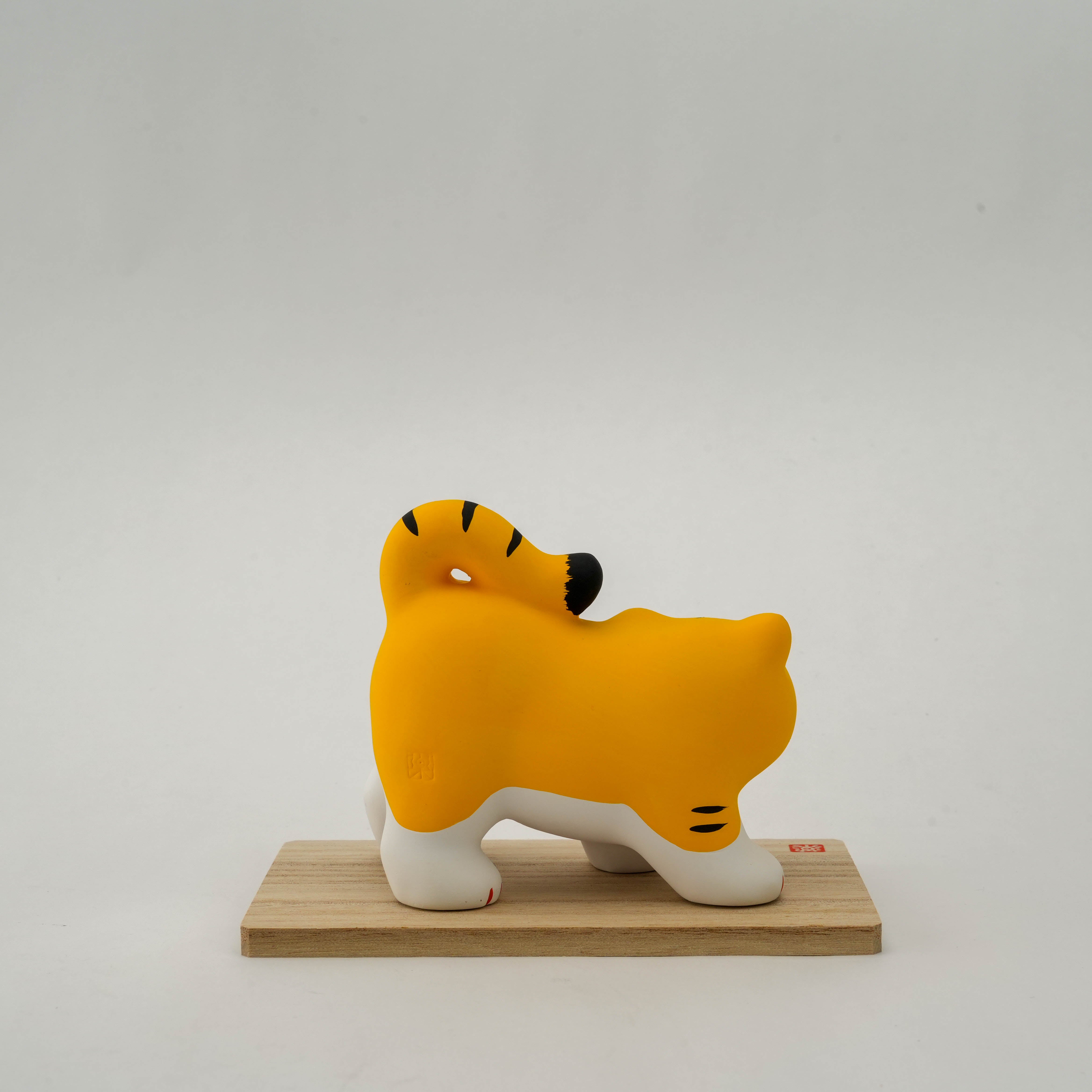 Rear view of Yakushigama Tiger Ornament highlighting the smooth ceramic finish and curled tail design on a wooden display base.