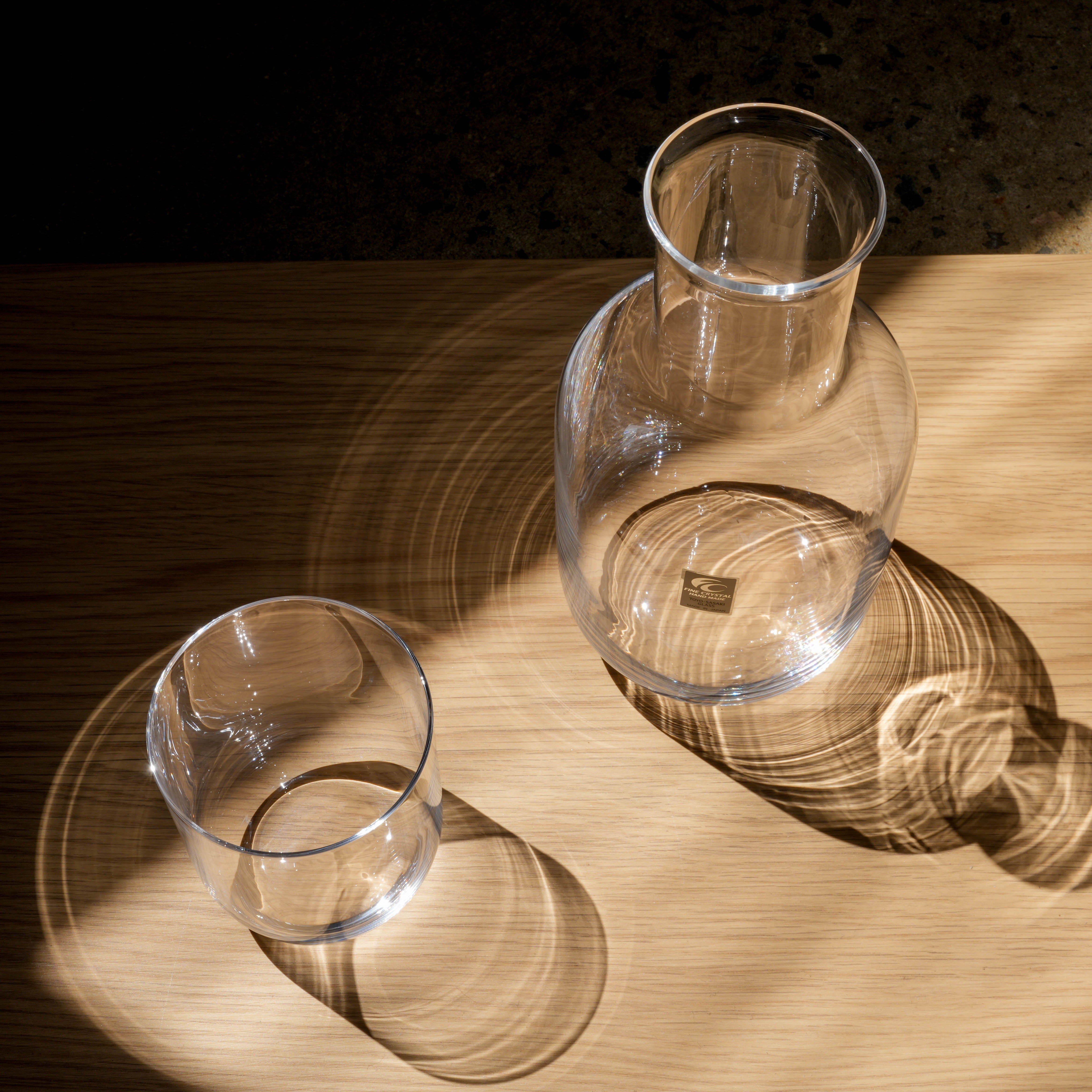 Toyo-Sasaki Night Carafe set with carafe and glass cup, casting elegant light reflections on wood surface, perfect for night hydration.