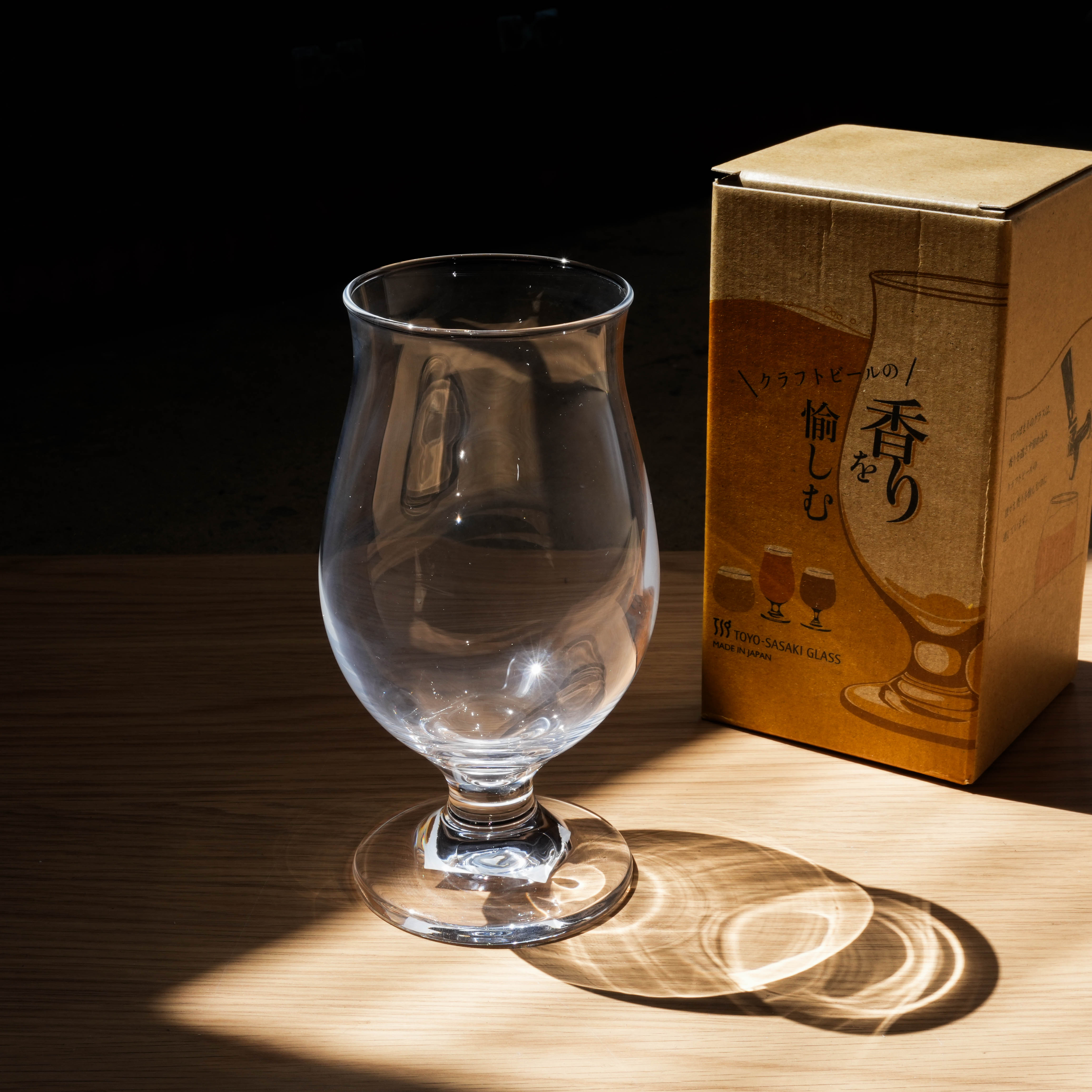Toyo-Sasaki Clear Tulip Beer Glass in dramatic lighting beside Japanese packaging, showcasing premium craft beer glassware.