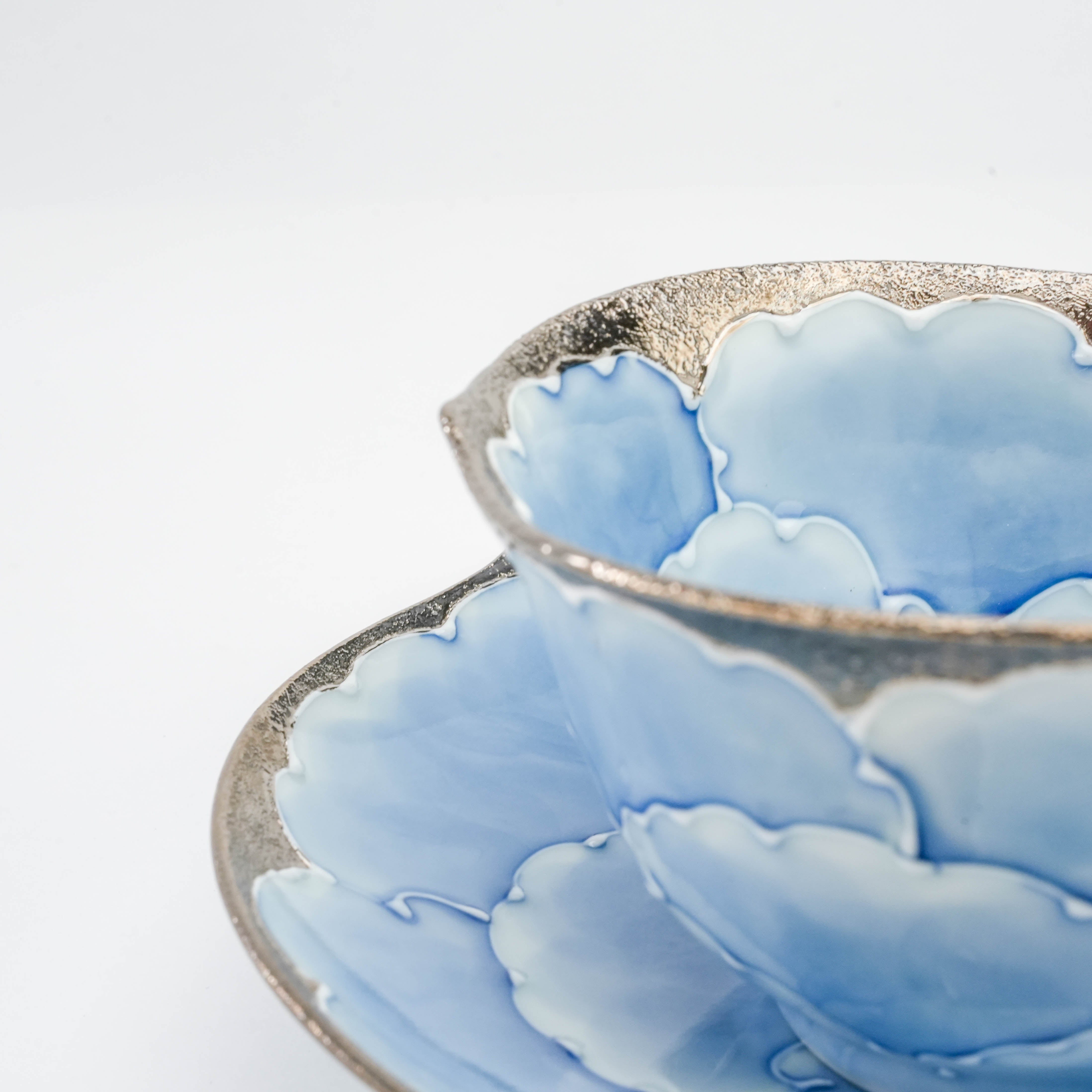 Macro shot of the Bunzan Kiln Cup & Saucer set's silver-edged rim and hand-painted blue peony petals, emphasizing artisanal detail.