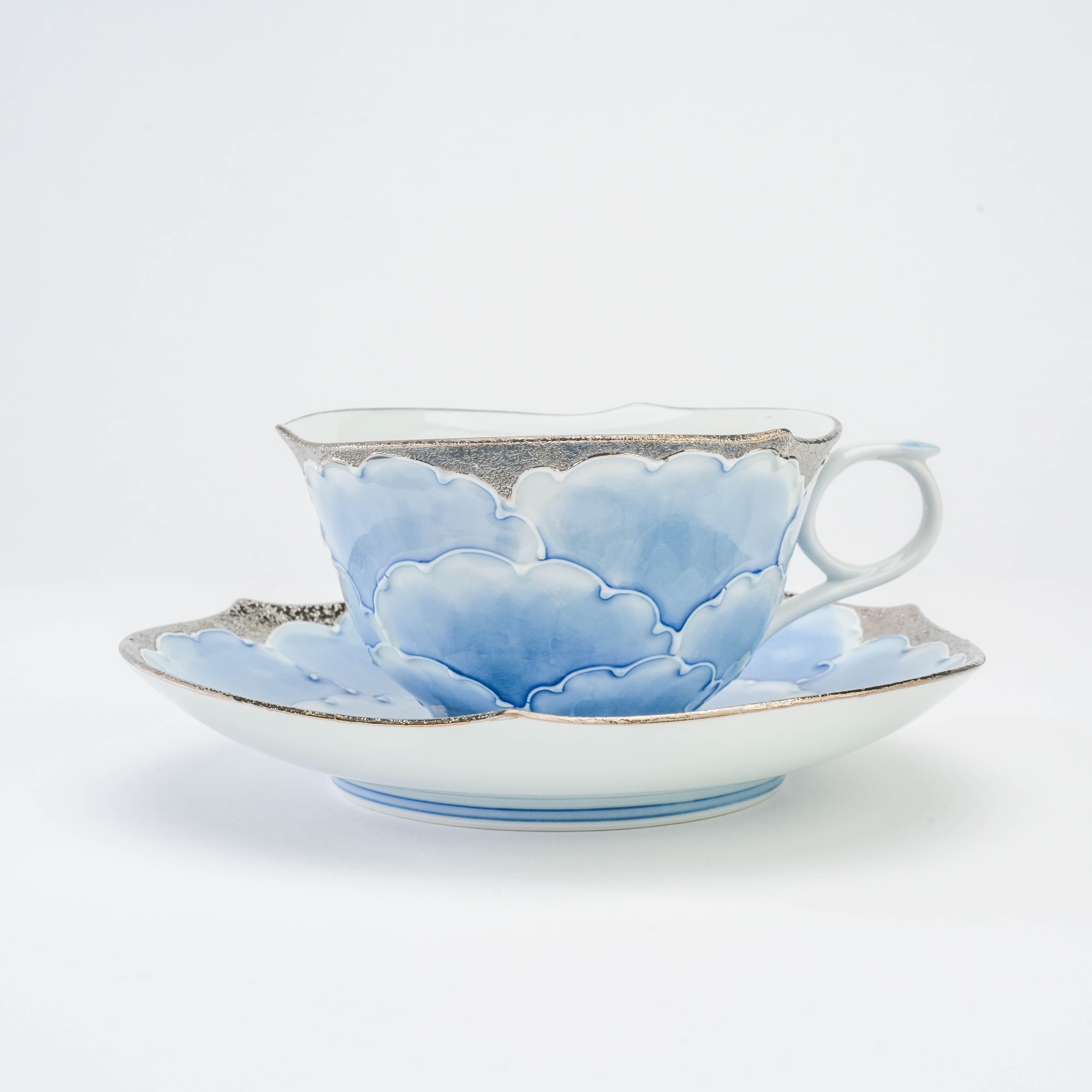 Side view of Bunzan Kiln Arita Peony Cup & Saucer set with layered blue petals and elegant silver detailing, ideal for refined tea service.