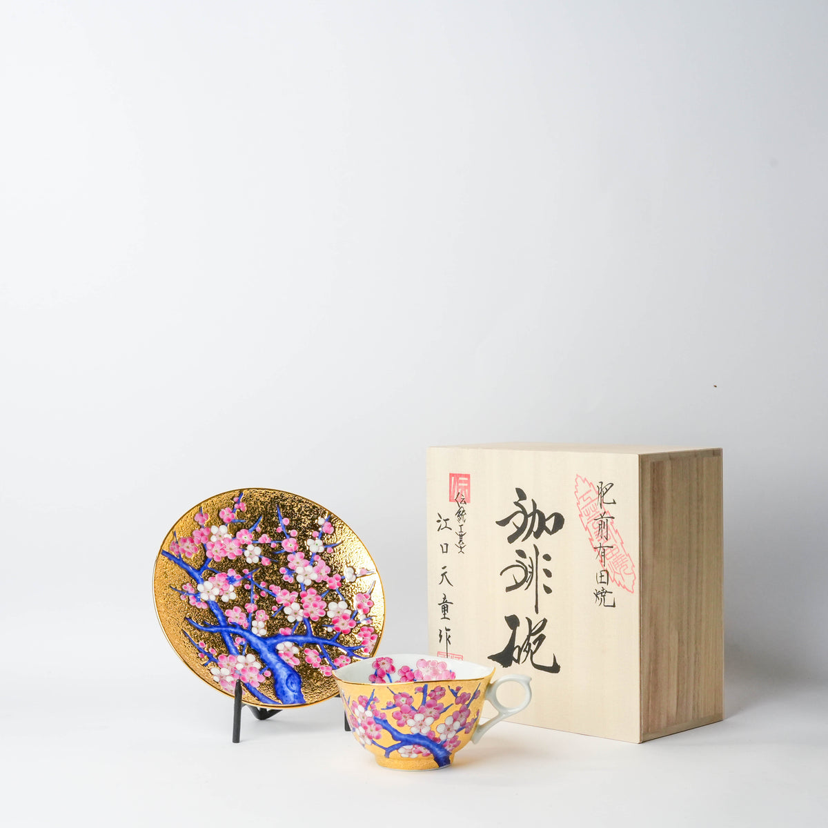 Close-up of a decorated teacup with pink plum blossoms, gold trim, and a matching saucer, showcasing intricate hand-painted details.
