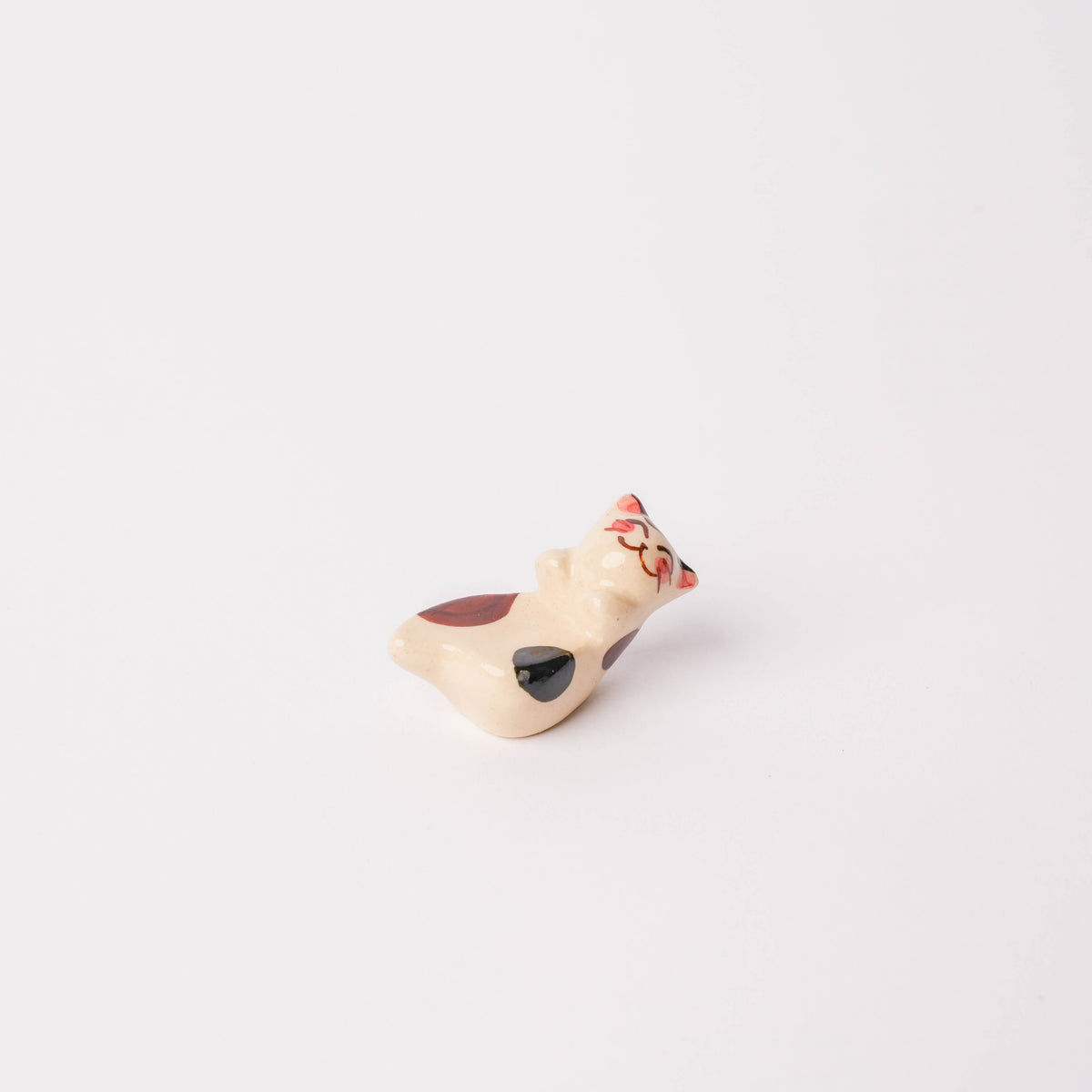 Close-up of the ceramic cat chopstick rest with painted facial features and striped pattern, on a white background