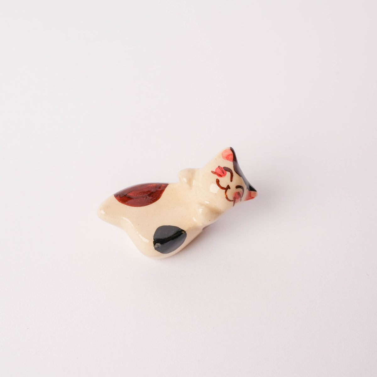 Ceramic cat chopstick rest with hand-painted details, showing playful expression and striped pattern, on white surface