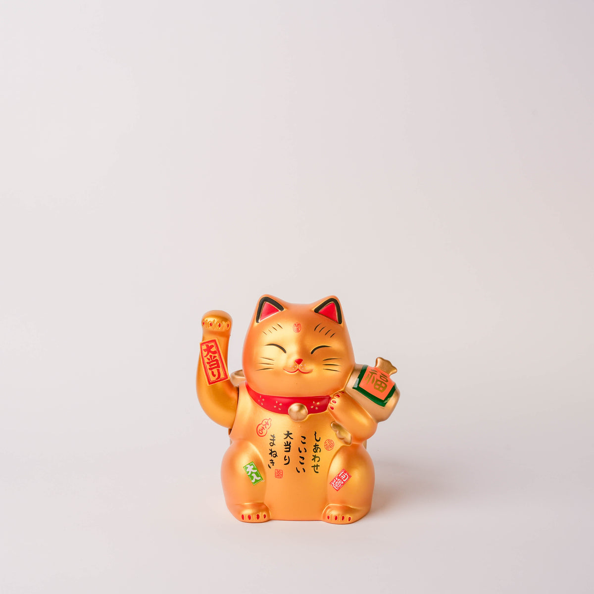 Gold Lucky Cat figurine with a smiling face, raised paw, and Japanese characters on its body, symbolizing good fortune and prosperity