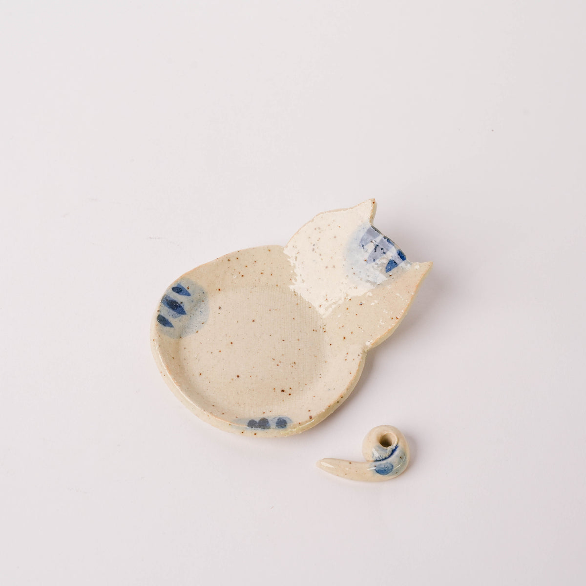 Side view of ceramic cat incense holder showing the cat's face and curled tail, beige with blue details, on a white surface.