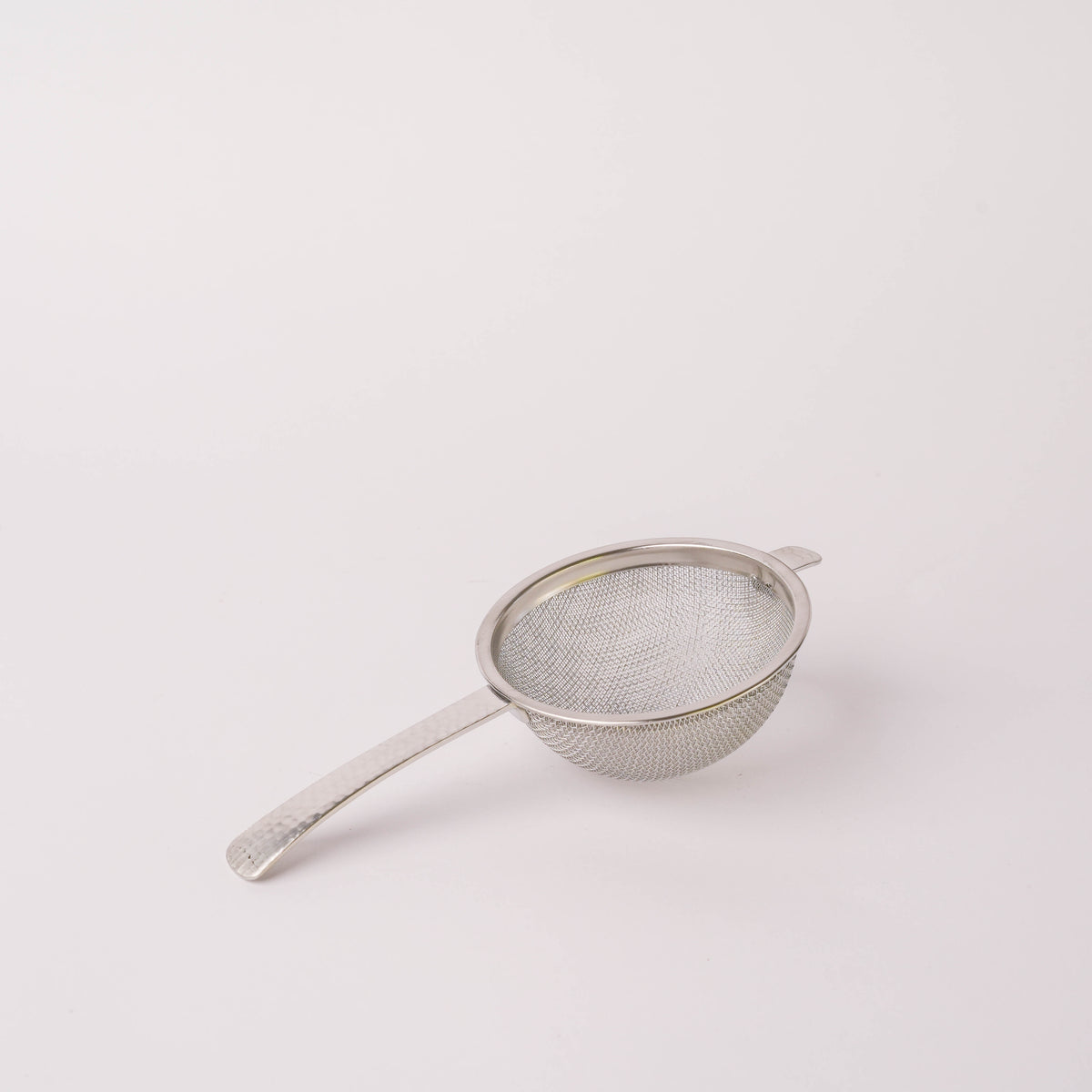 Stainless steel hammered tea strainer with fine mesh, round shape, and long handle, ideal for brewing loose leaf tea in kitchen or dining setting