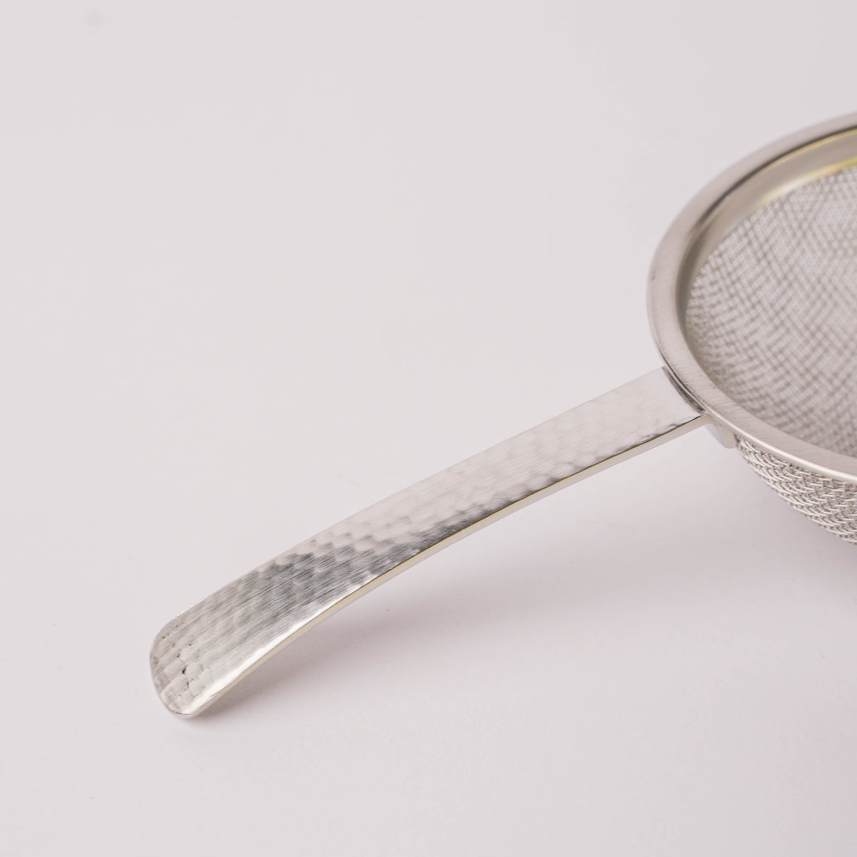 Bottom view of stainless steel hammered tea strainer with mesh surface and curved handle, designed for effortless tea filtering in home or restaurant use