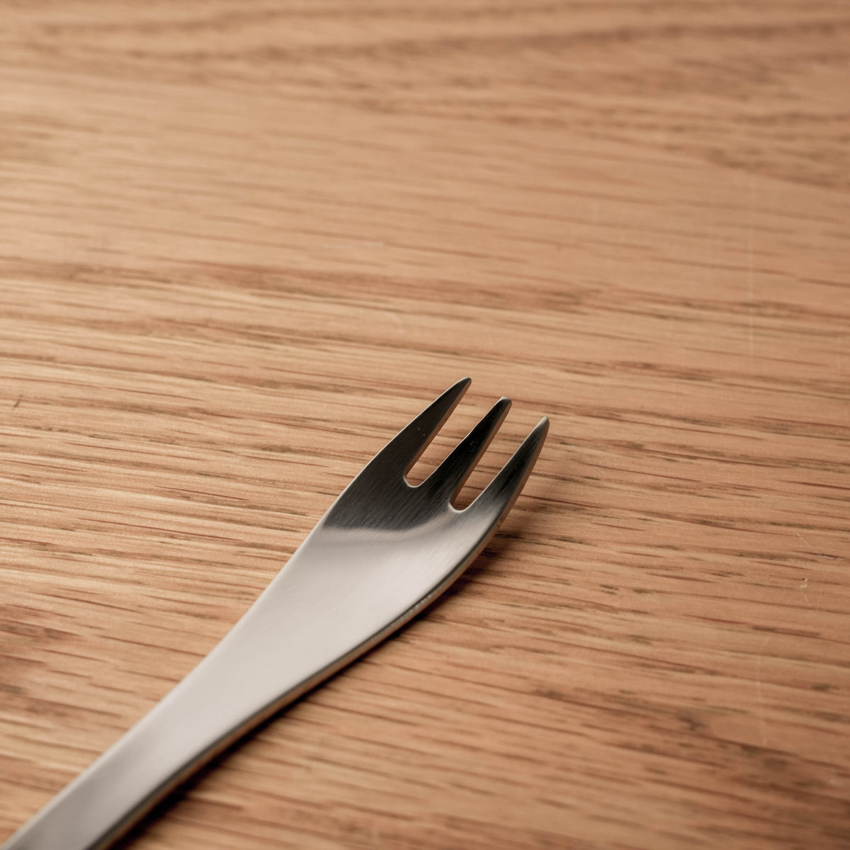 Close-up of the stainless steel fork's handle, showing its sleek, weighted design, on a wooden background.