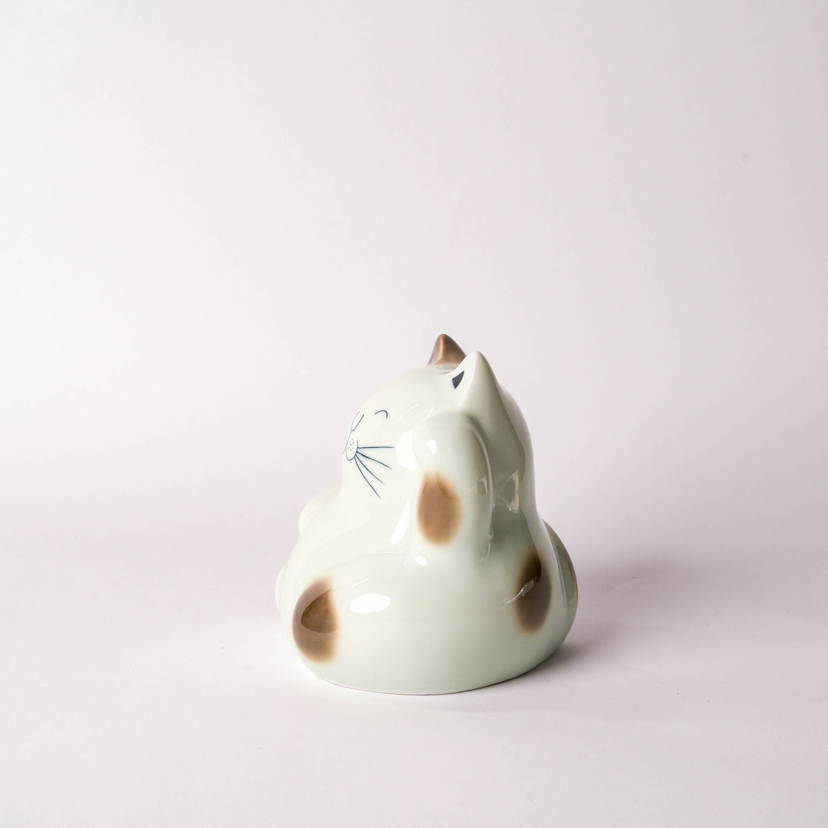 Close-up of ceramic cat figurine showing its face with black eyes, nose, and whiskers, on a white background, decorative home accessory