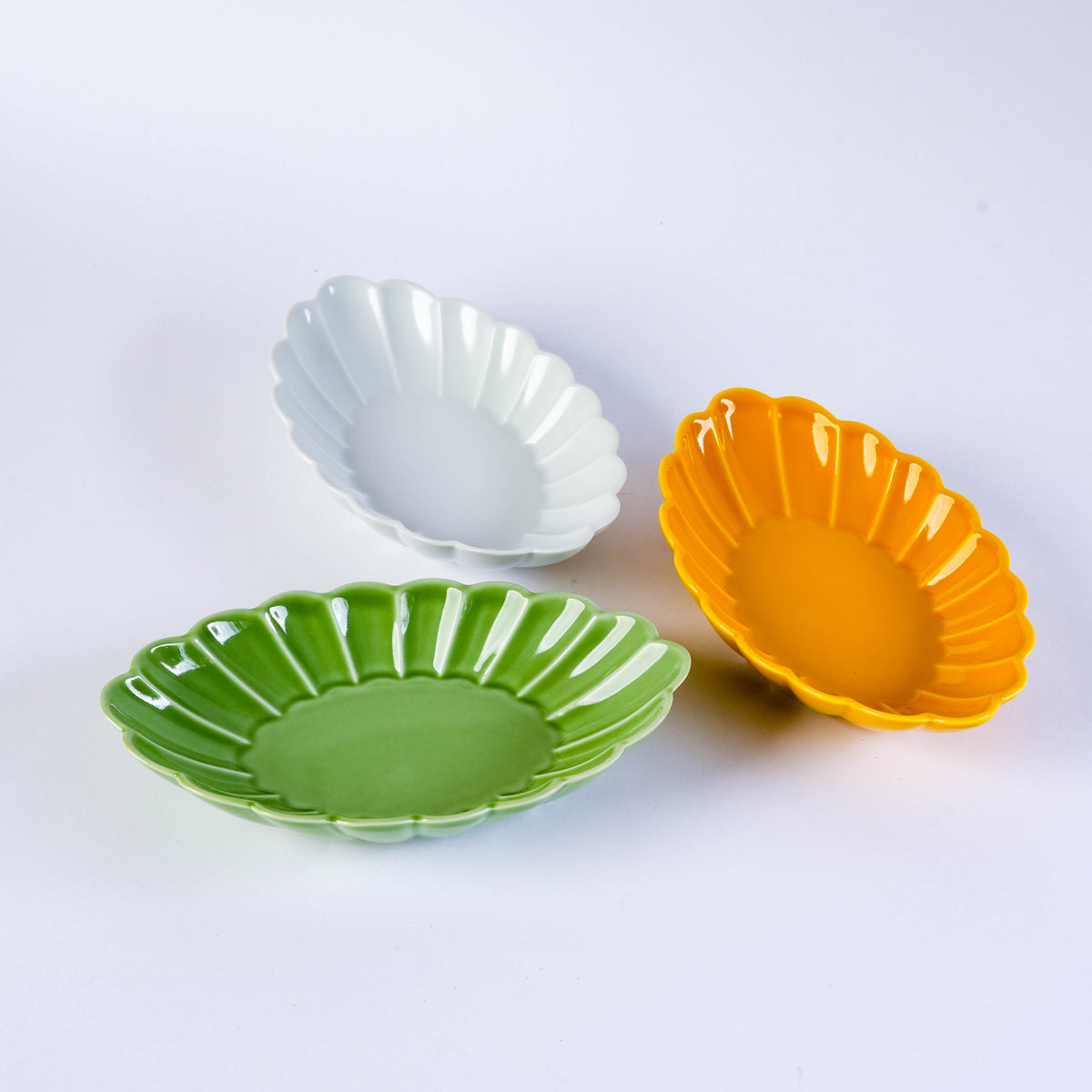 Orange ceramic oval plate with scalloped edges and carved leaf design, suitable for serving snacks or desserts, on a white background
