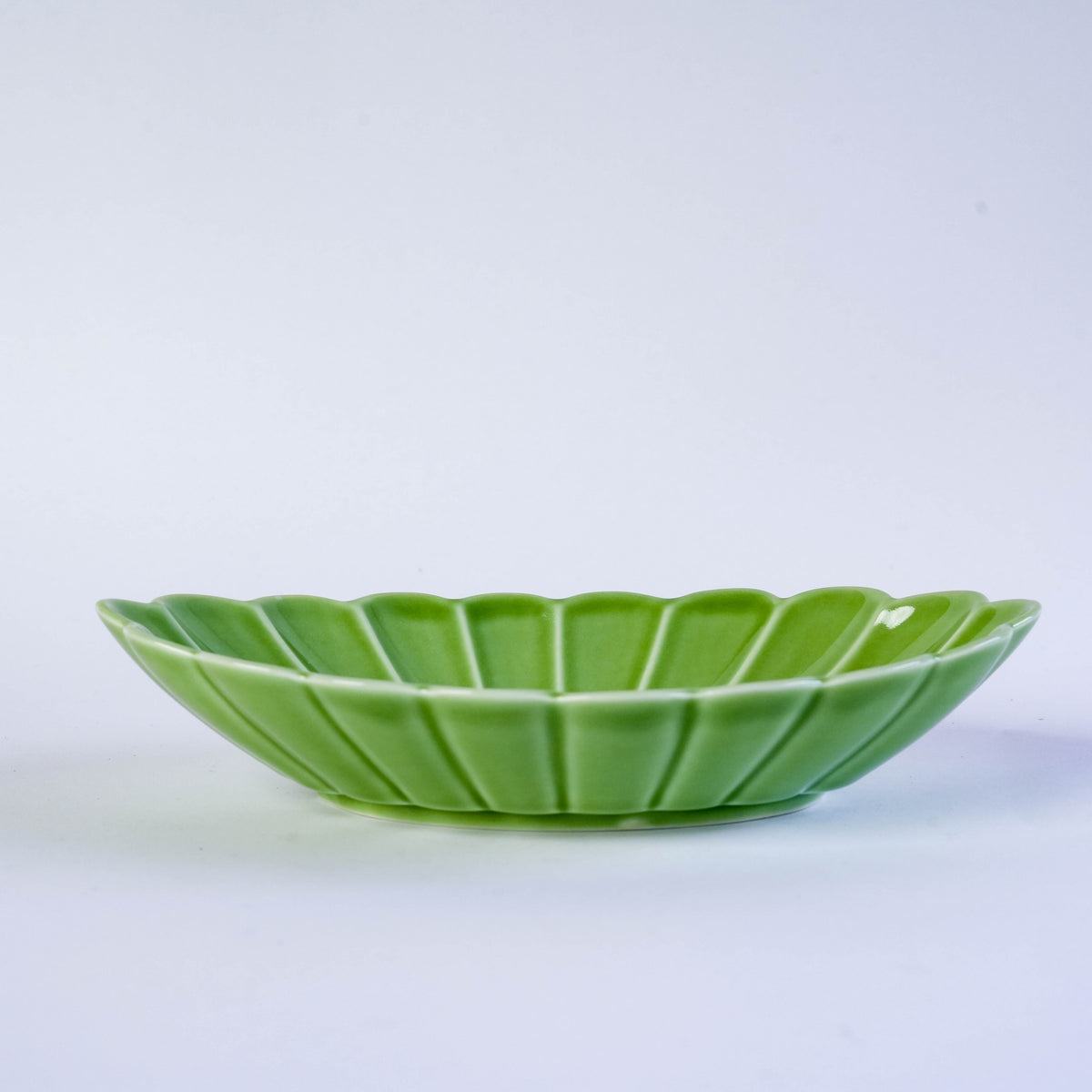 Green ceramic oval plate with carved leaf design, perfect for serving appetizers or desserts, on a white background