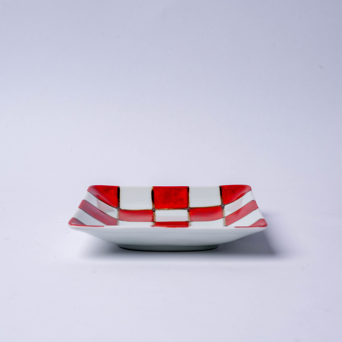 Side view of a square Japanese porcelain plate with red and blue checkered pattern, suitable for serving snacks or sweets