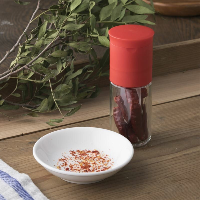 Kai Home Ceramic Red Pepper Mill on a wooden kitchen counter with ground pepper flakes in a dish, perfect for seasoning meals.