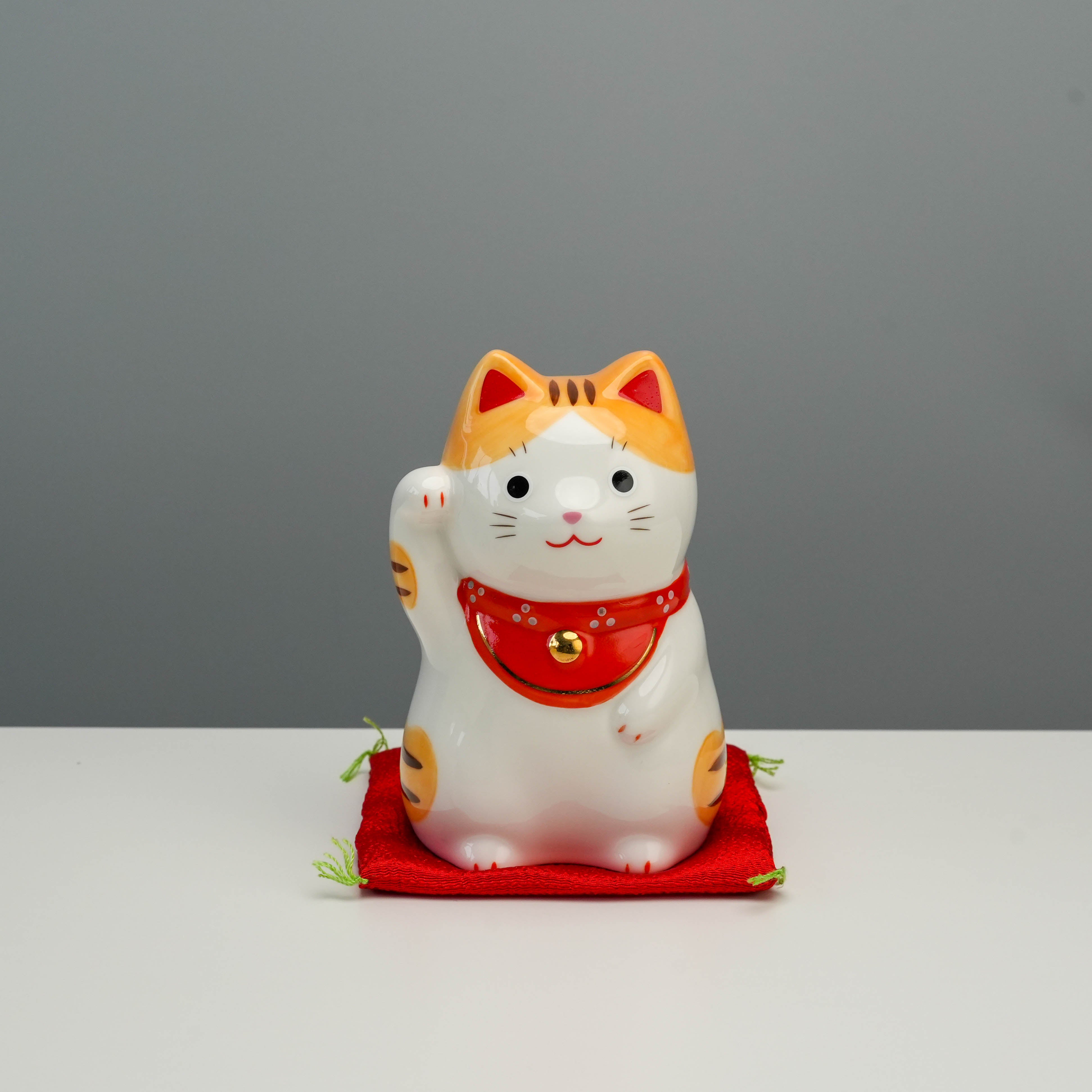 Yakushigama Lucky Cat - Japanese Fortune Charm in orange tiger design, seated on red cushion, ideal for home decor and prosperity attraction.