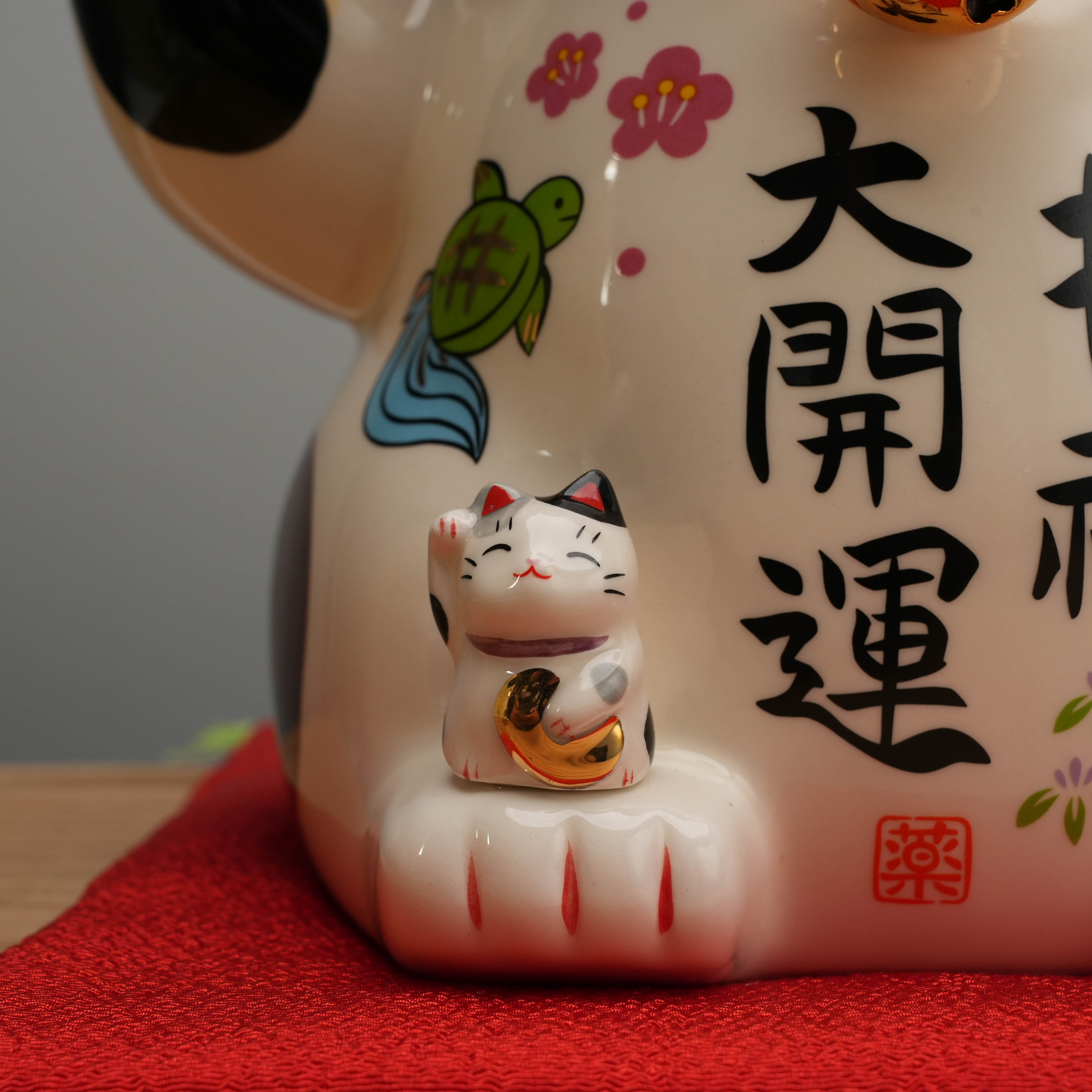 Close-up of small beckoning cat on Yakushigama Bliss figurine’s paw, enhancing the charm and symbolism of prosperity in home decor.