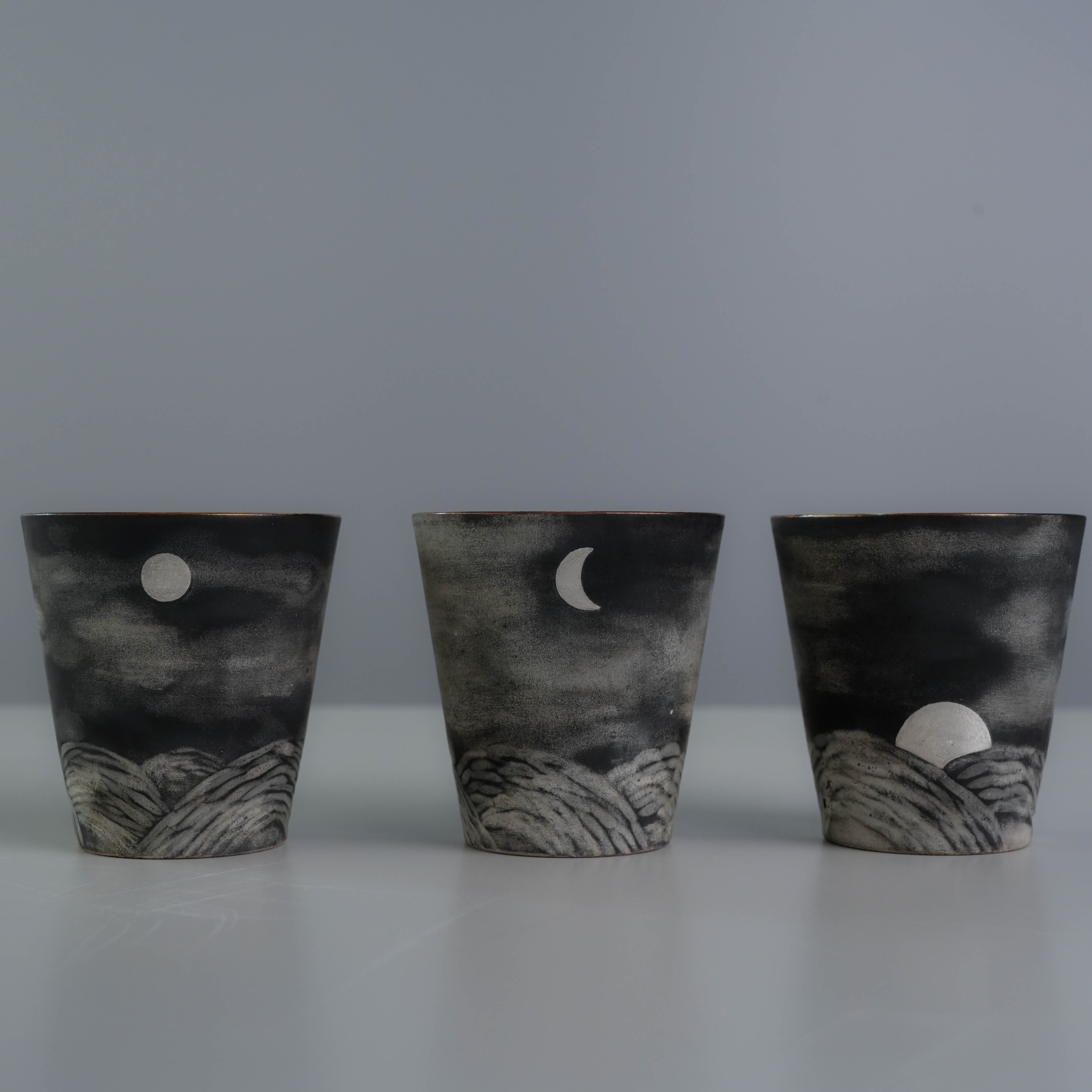 Three Lonesome Studio Qushui tea cups with moon phase designs and mountain motifs, handmade with silver glaze for Gongfu Cha tea ceremonies.