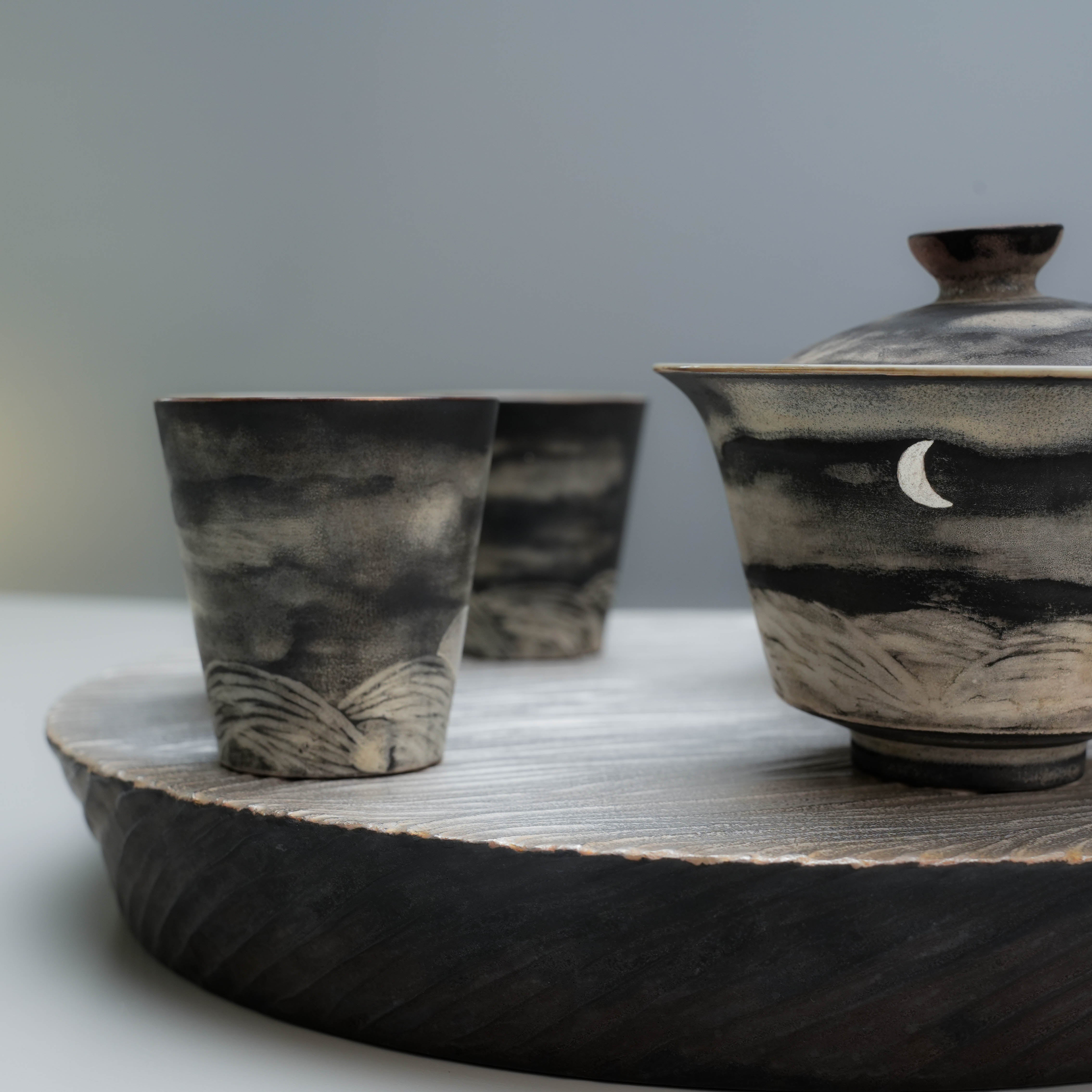 Close-up of Lonesome Studio Qushui gaiwan and tea cups with crescent moon design, handmade with silver glaze for Gongfu Cha tea rituals.
