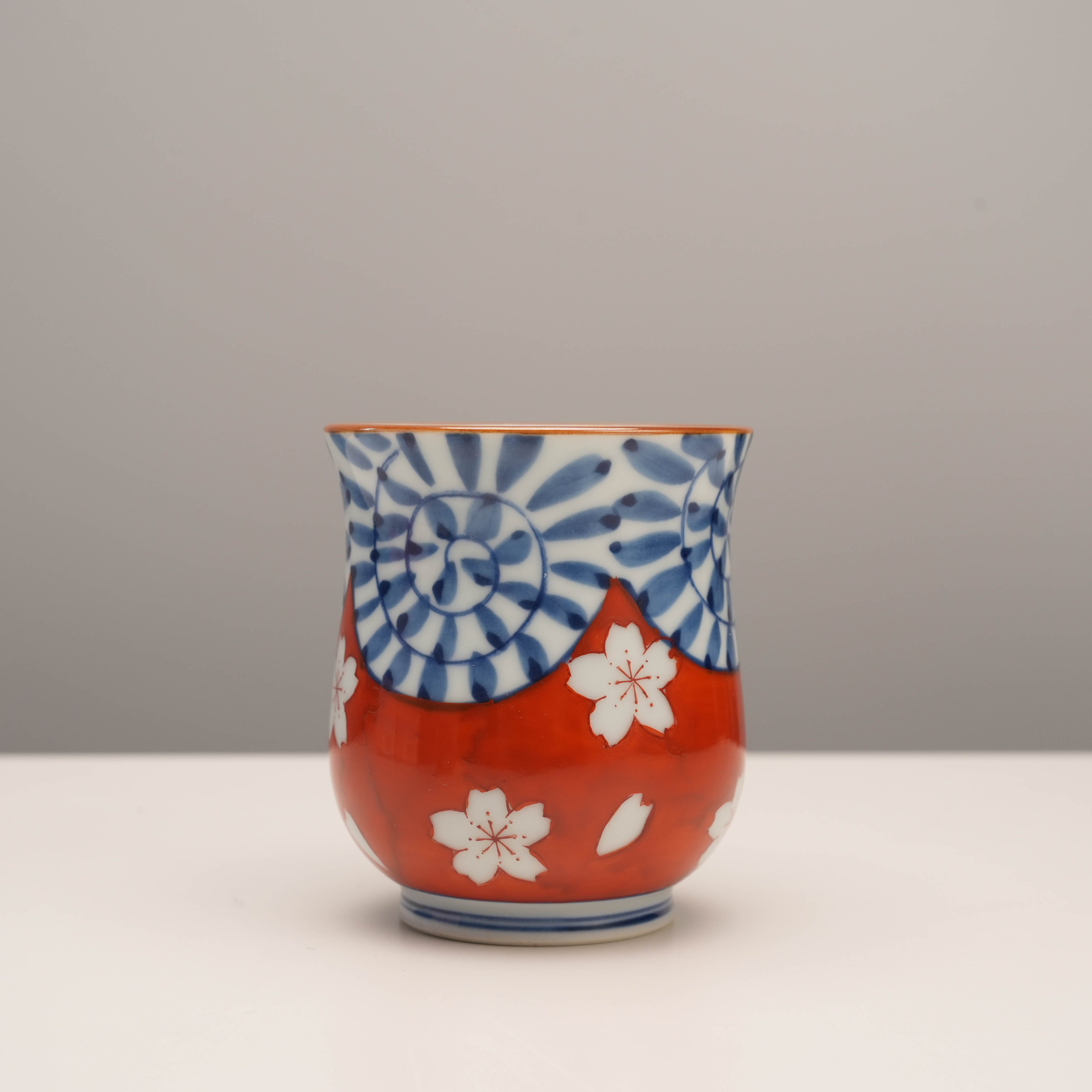 Red Arita Ware Yunomi tea cup with blue arabesque and white cherry blossom accents. Durable hand-painted Japanese porcelain.