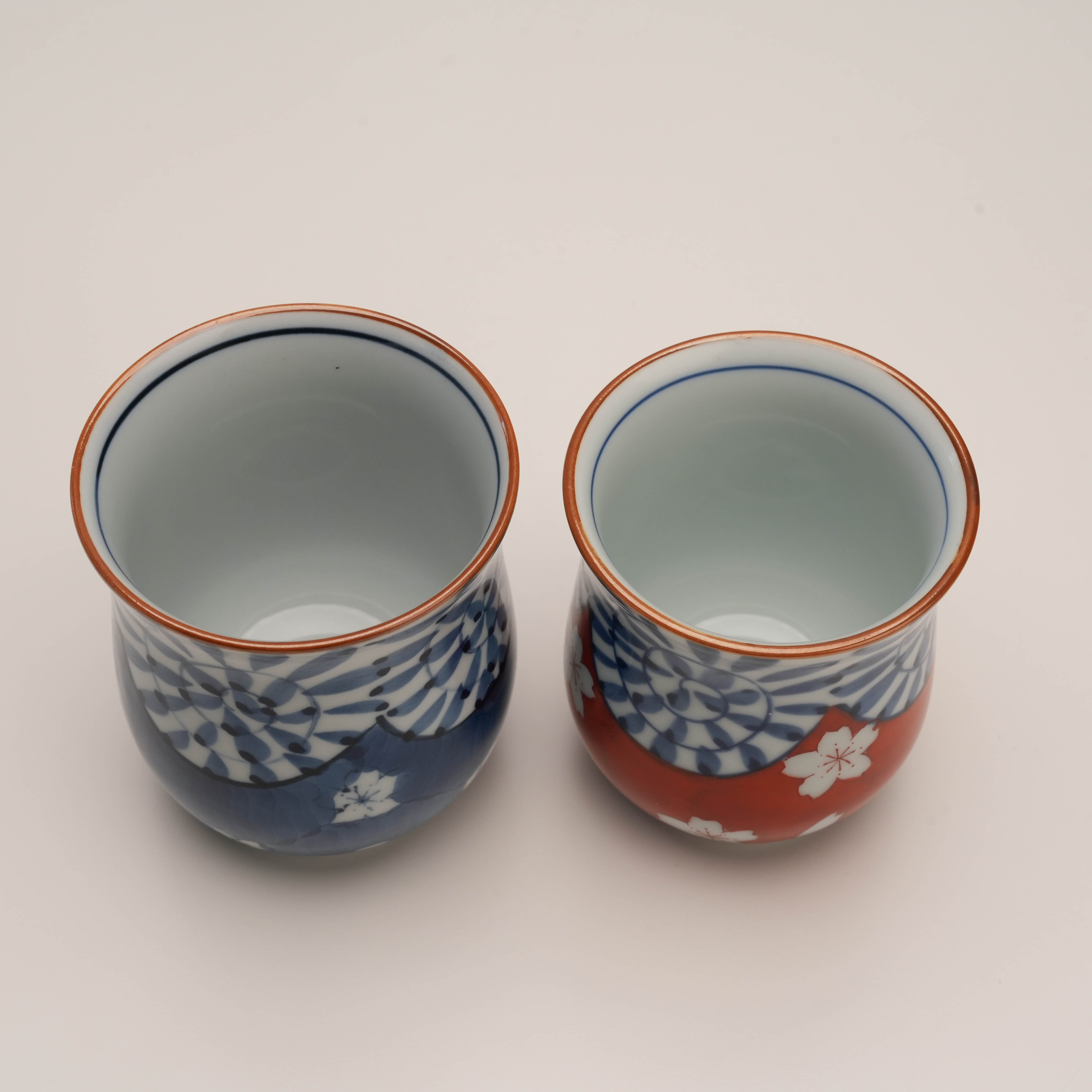 Top view of blue and red Arita Ware Yunomi tea cups. Hand-painted Japanese porcelain with floral and spiral motifs for elegant tea enjoyment.