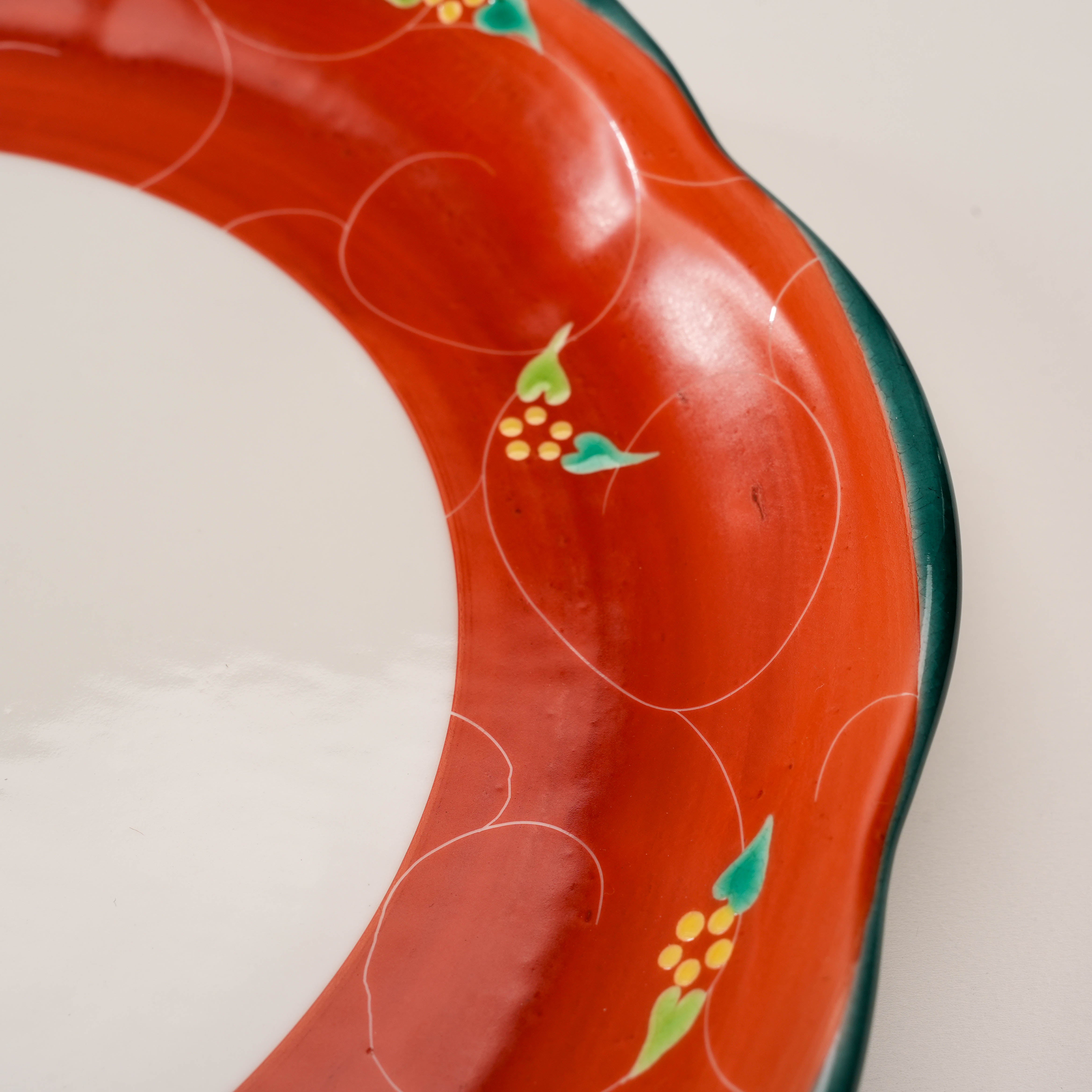 Close-up of Kutani Ware Plate's vermilion arabesque border with intricate floral detailing and smooth scalloped edges.