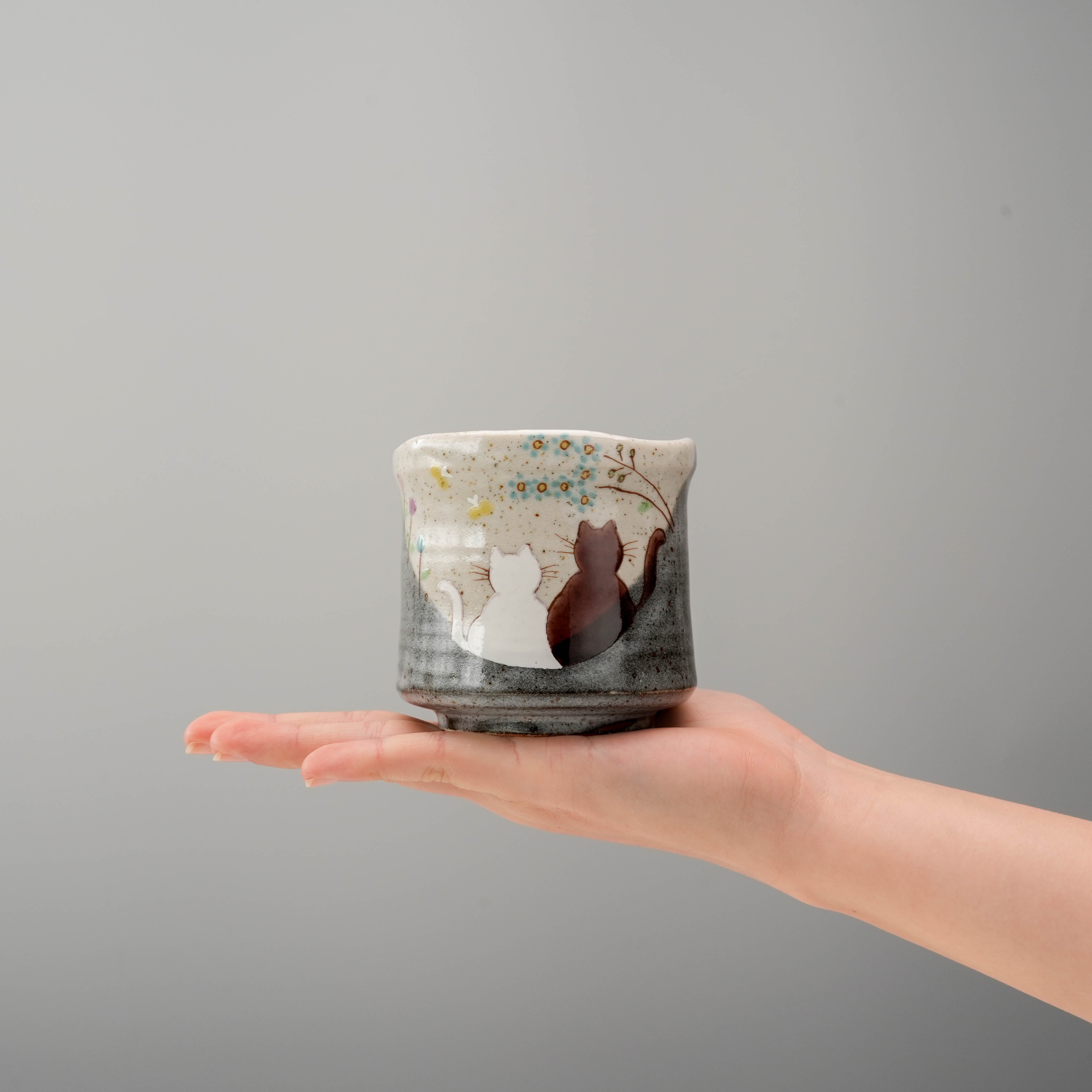 Handcrafted Kutani Ware Yunomi Teacup shown in hand for scale, highlighting its charming cat design and artisanal ceramic texture.