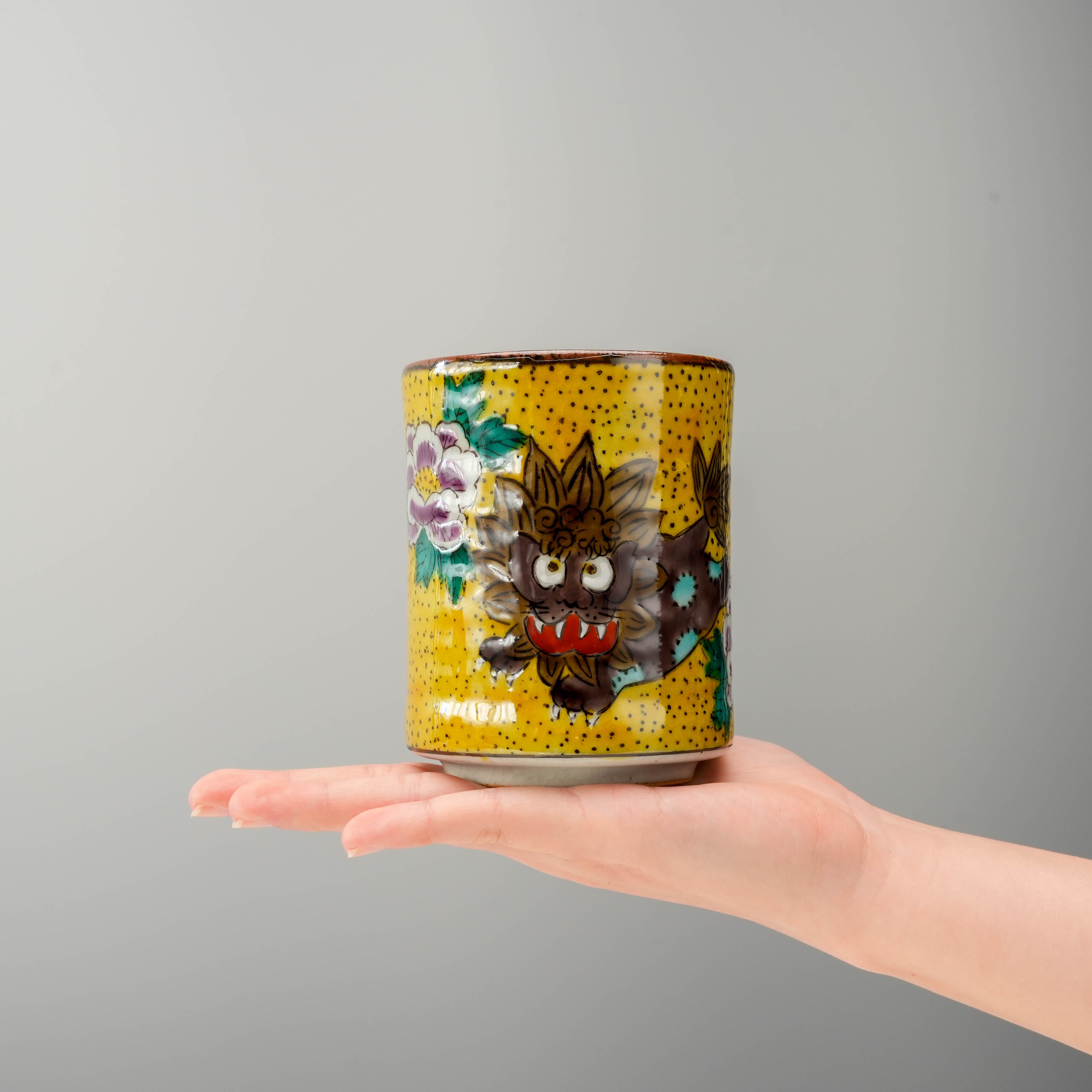Hand holding Kutani Ware Guardian Lion & Peony Teacup, showcasing its size and detailed Karajishi design in vibrant traditional Japanese colors.