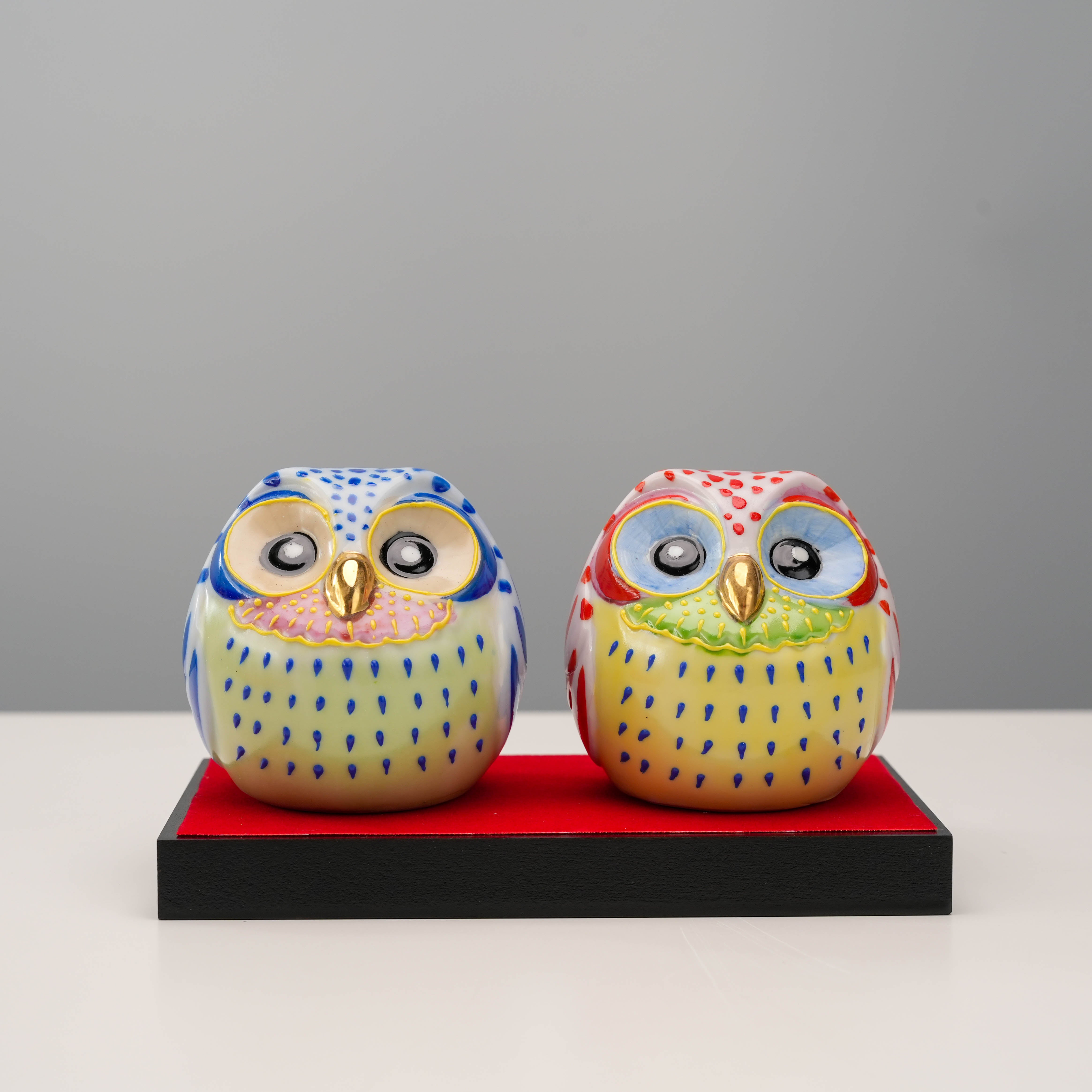 Kutani Owl Pair - Lucky Ornament featuring hand-painted blue and red owls with golden beaks on a red display base. Ideal for home decor or gifting.