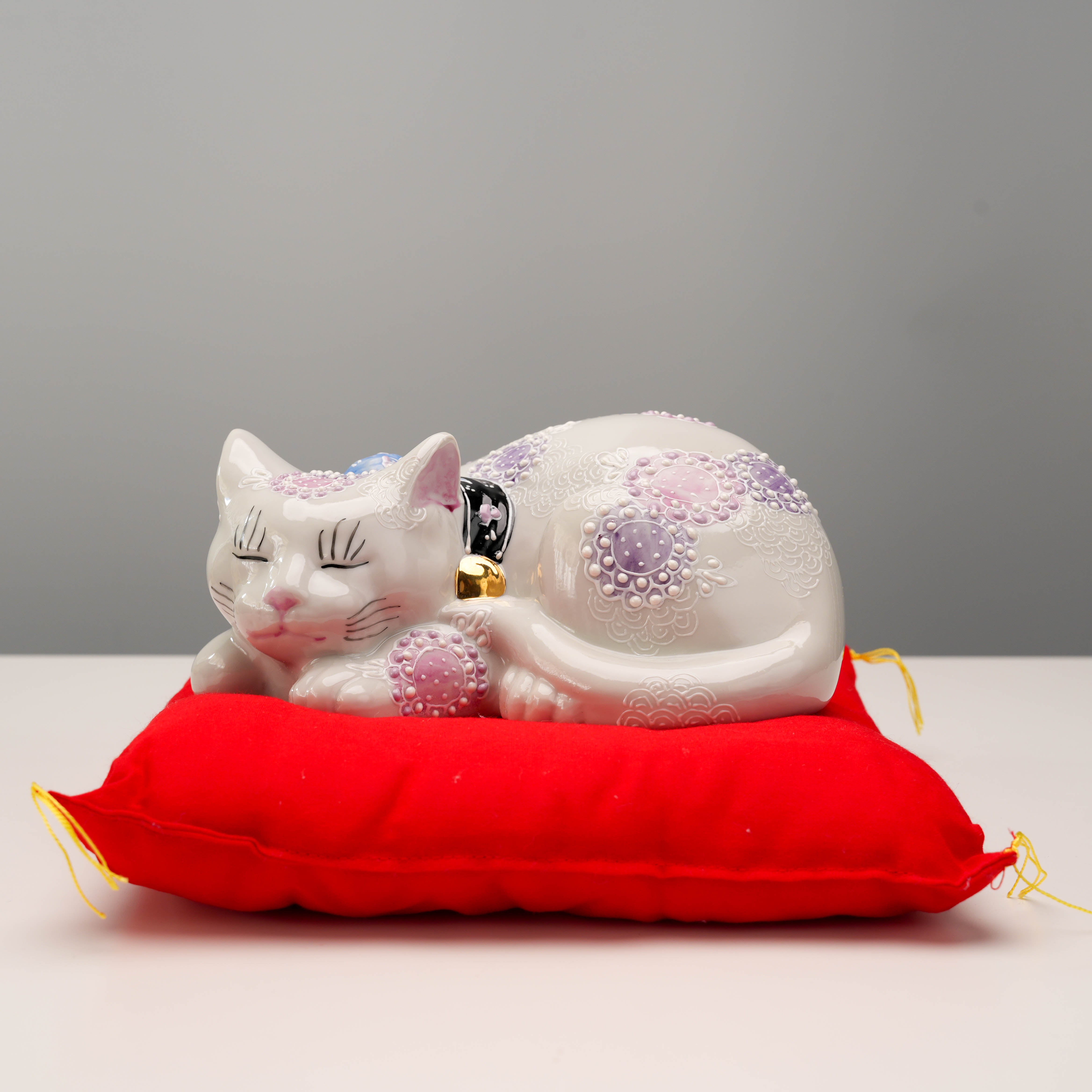 Kutani Ware Ornament Sleeping Cat - Lucky Cat with purple floral motifs resting on red cushion, ideal for home decor or gifting.