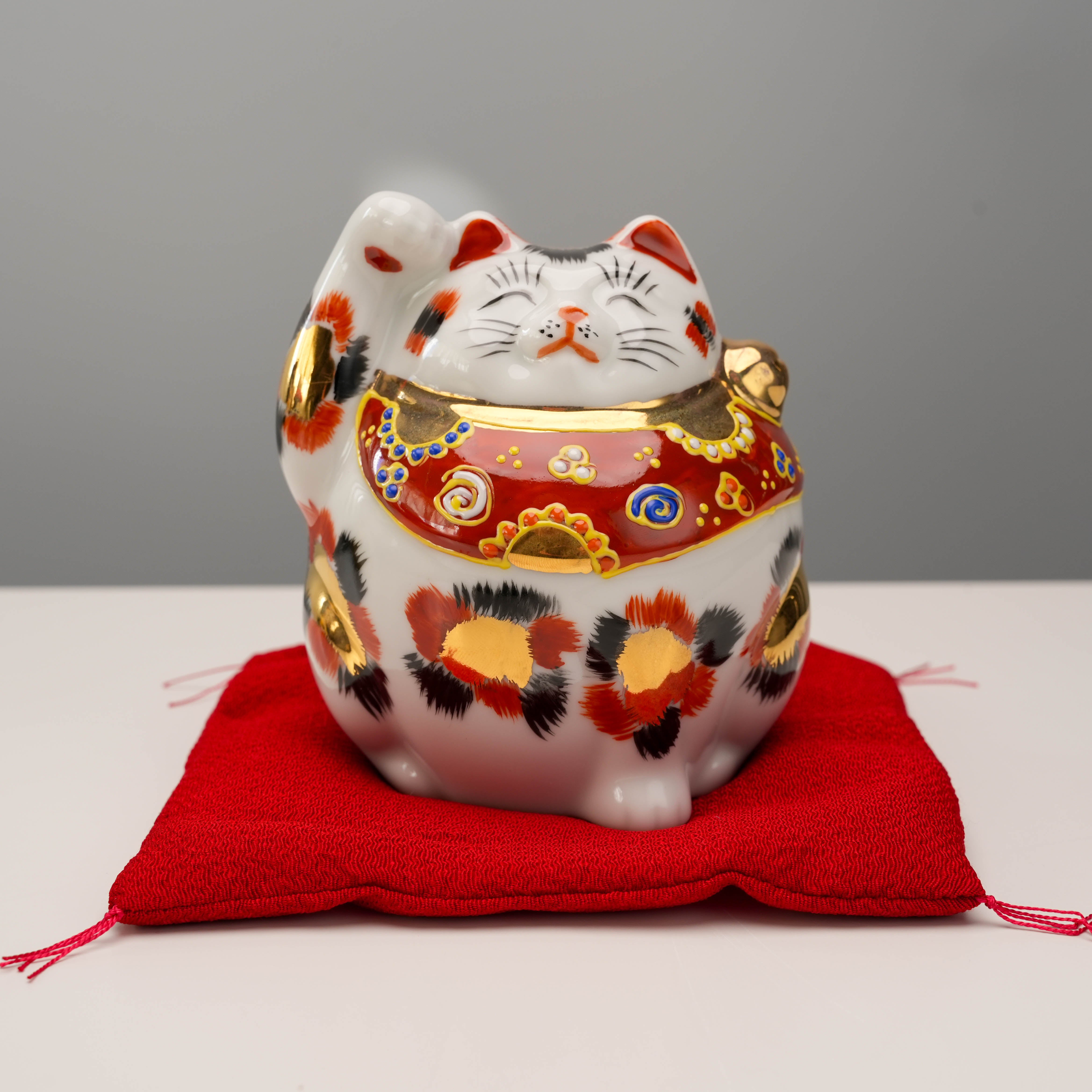 Kutani Ware Cat – Lucky Calico figurine with gold and red detailing, seated on a red cushion, symbolizing joy and prosperity.