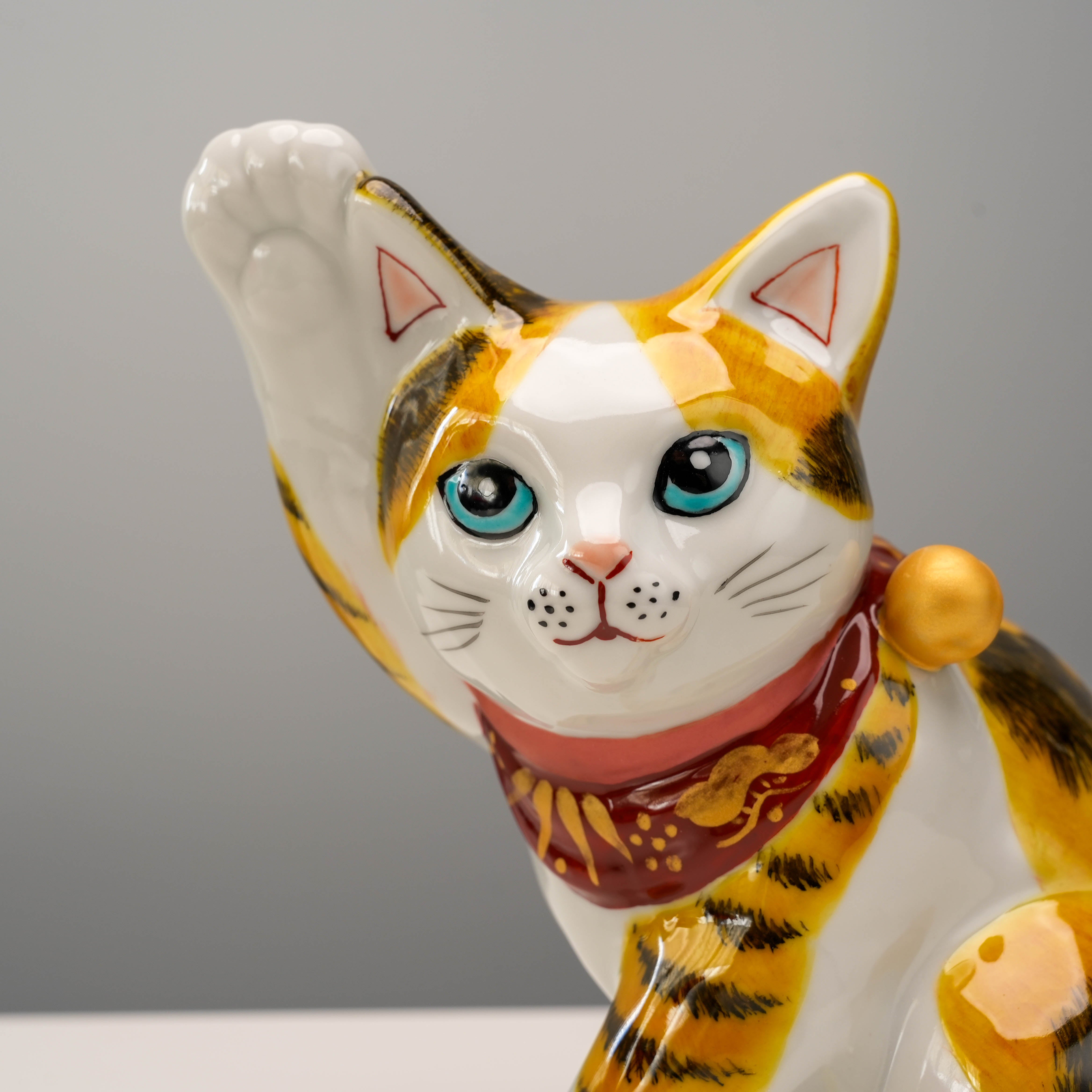 Close-up of Kutani Ware Lucky Cat figurine showing detailed blue eyes, red scarf, and raised paw in traditional Aokutani calico design.