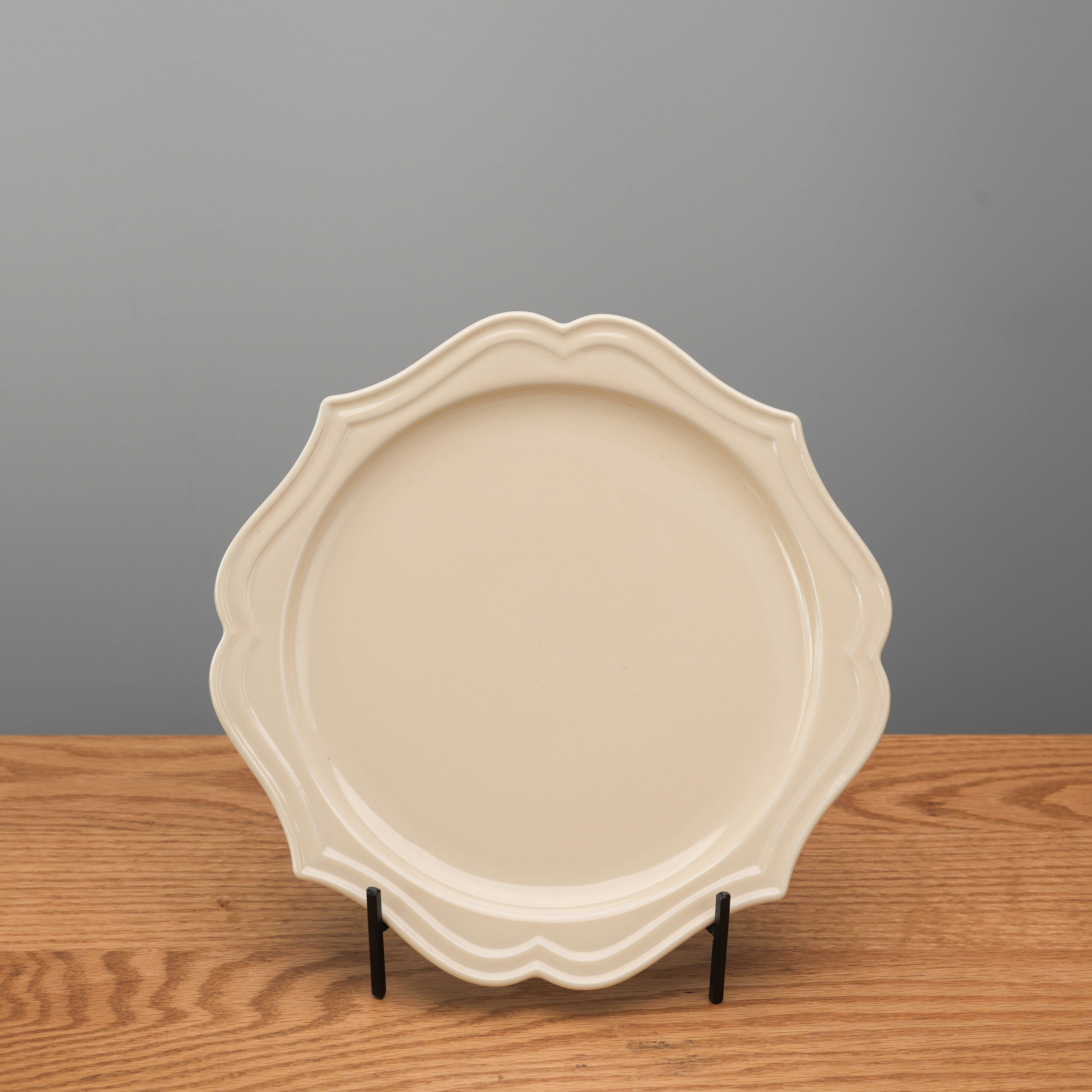 Helsinki Namako Plate - Round Plate with scalloped edge in beige, 23cm, displayed upright on wooden surface. Ideal for elegant dining settings.