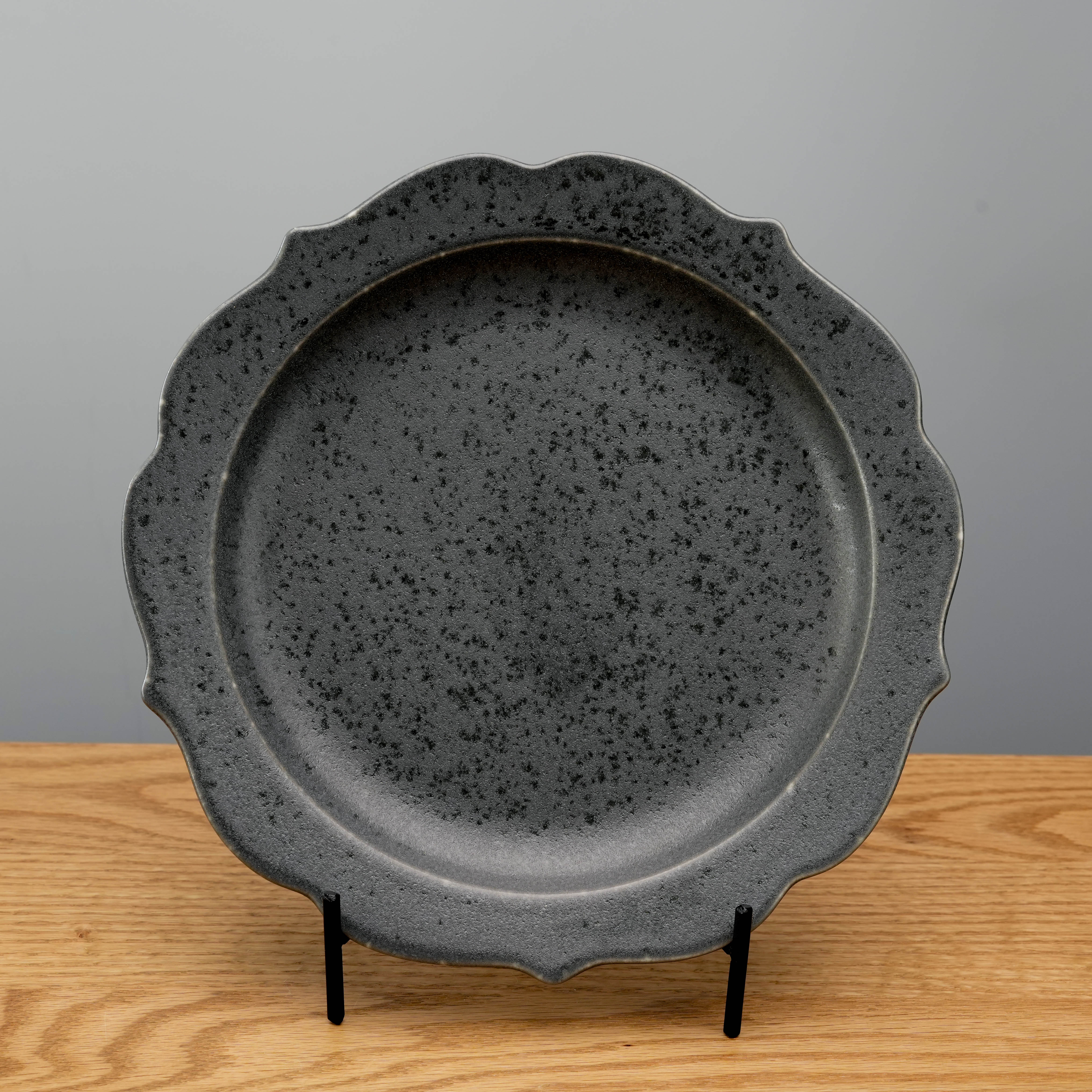 Kikyo Black Plate with scalloped edges in matte gray finish, displayed upright on wooden surface. Japanese-style Mino Ware for elegant dining.