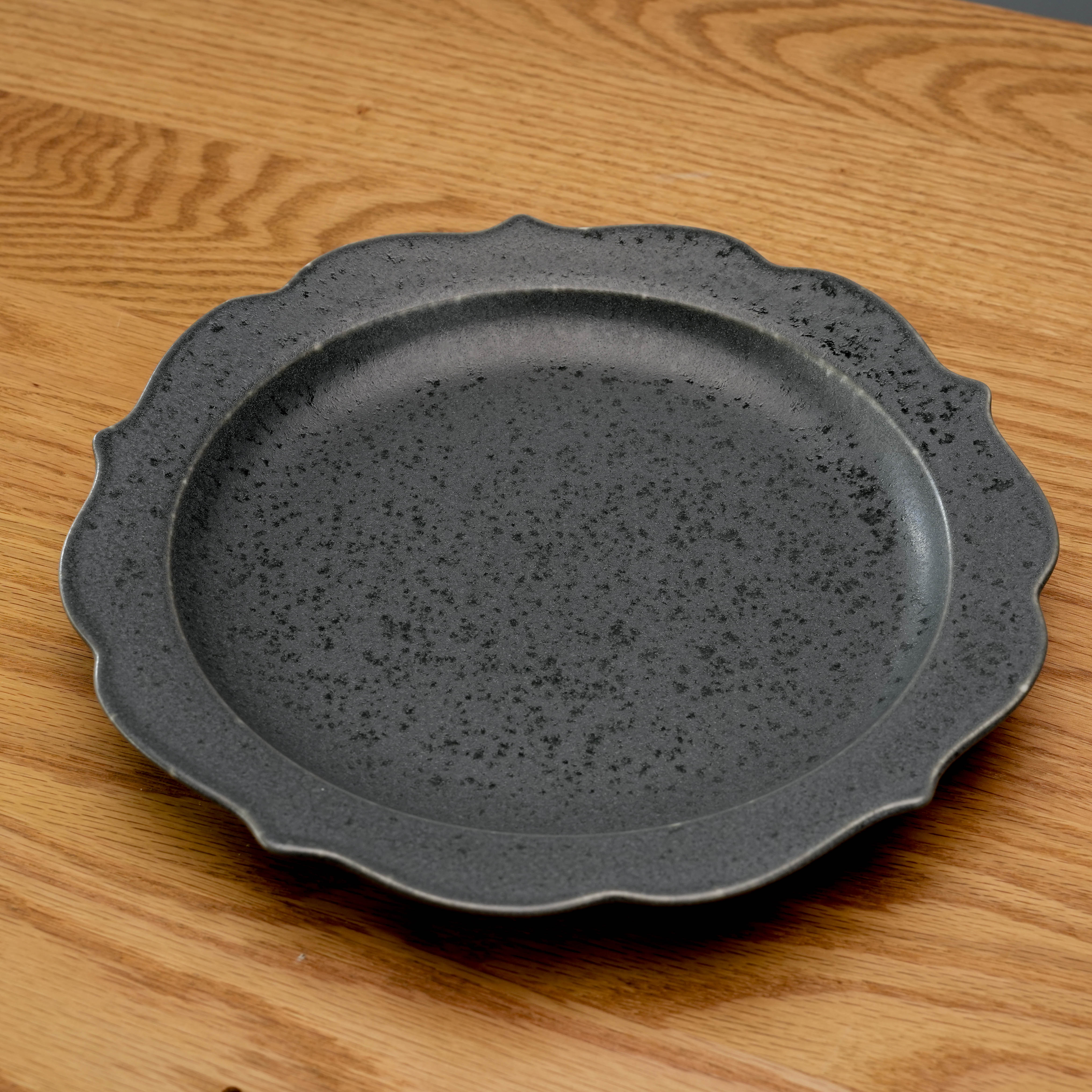 Minimal matte Kikyo Black Plate with speckled texture and wavy rim, lying flat on wood table. Ideal for modern Japanese table settings.