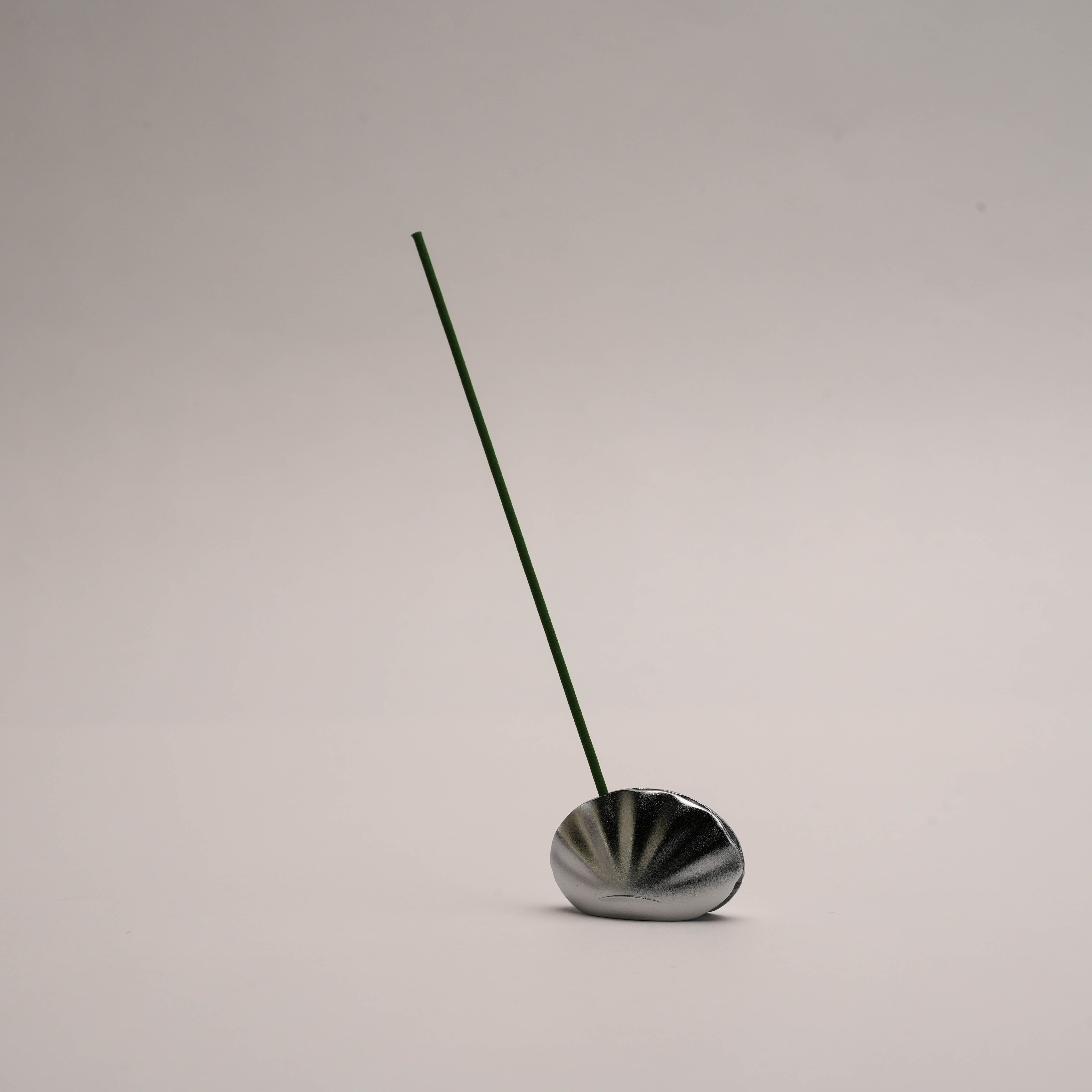 Shoyeido Kolip Shell Incense Holder in matte silver securely holding a stick of incense upright, ideal for stylish home fragrance setups.