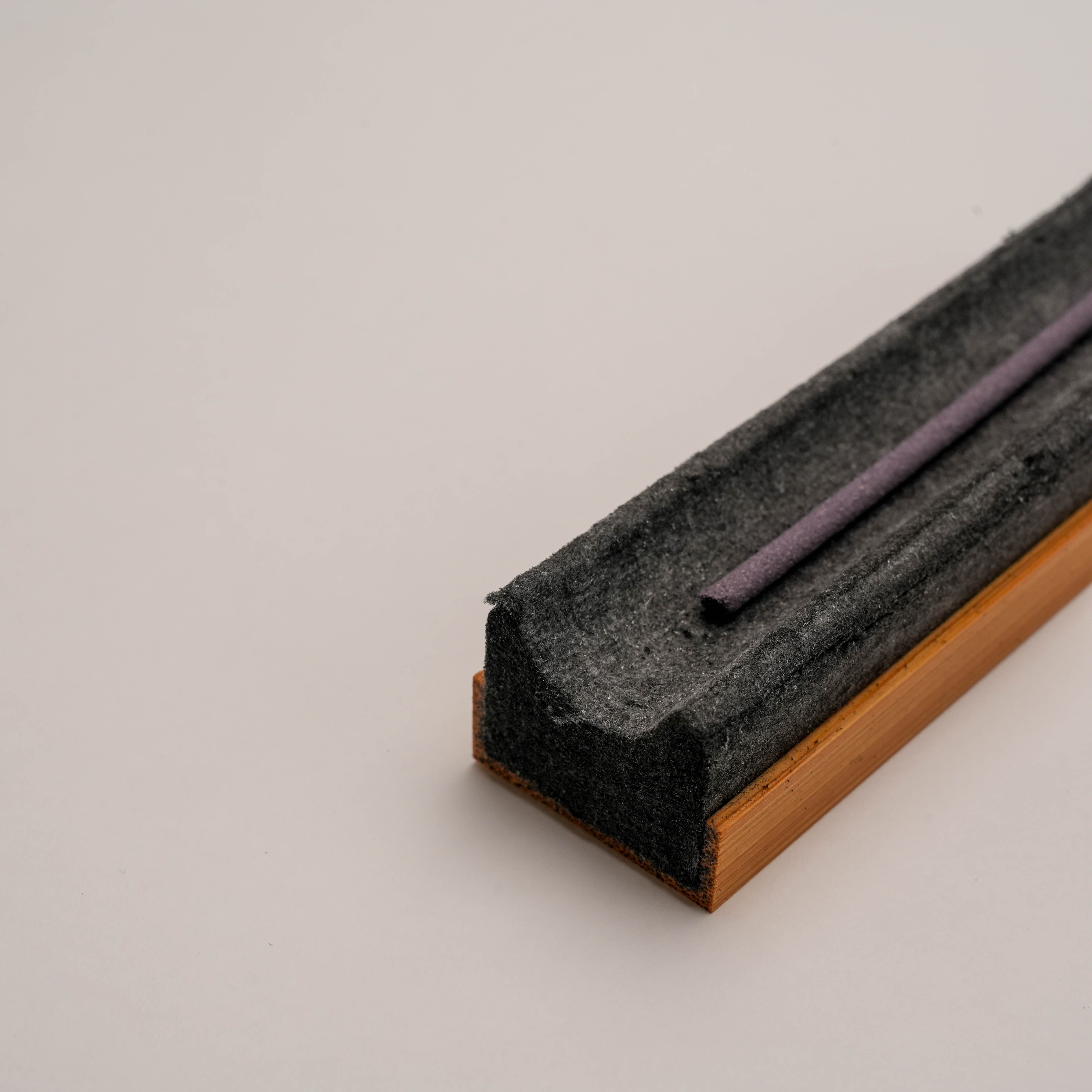 Close-up of Shoyeido Takuba incense tray holding a purple incense stick, highlighting its efficient ash-catching felt base.