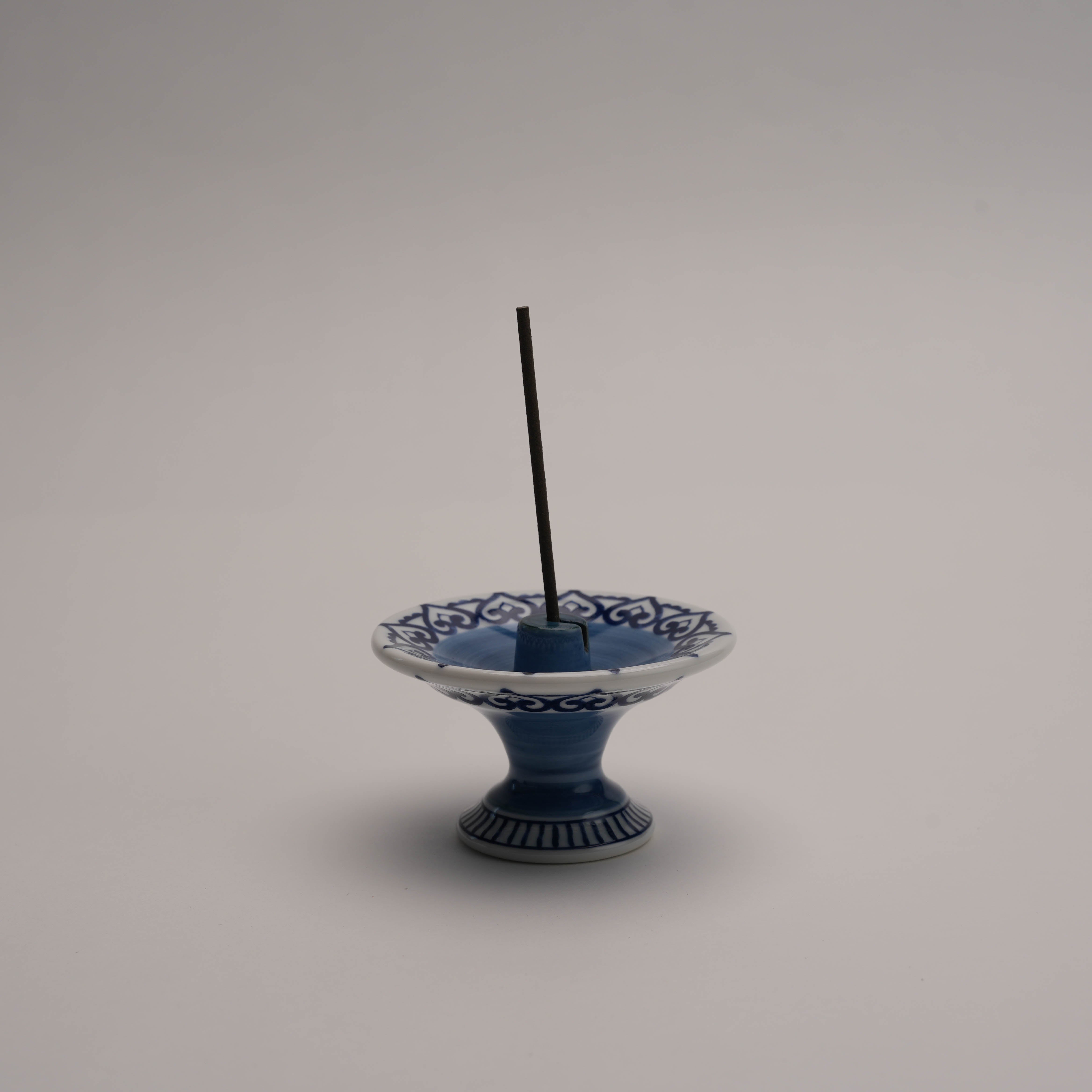 Shoyeido Arabesque Incense Burner holding a stick incense, showcasing its versatile use and elegant blue ceramic design for home rituals.