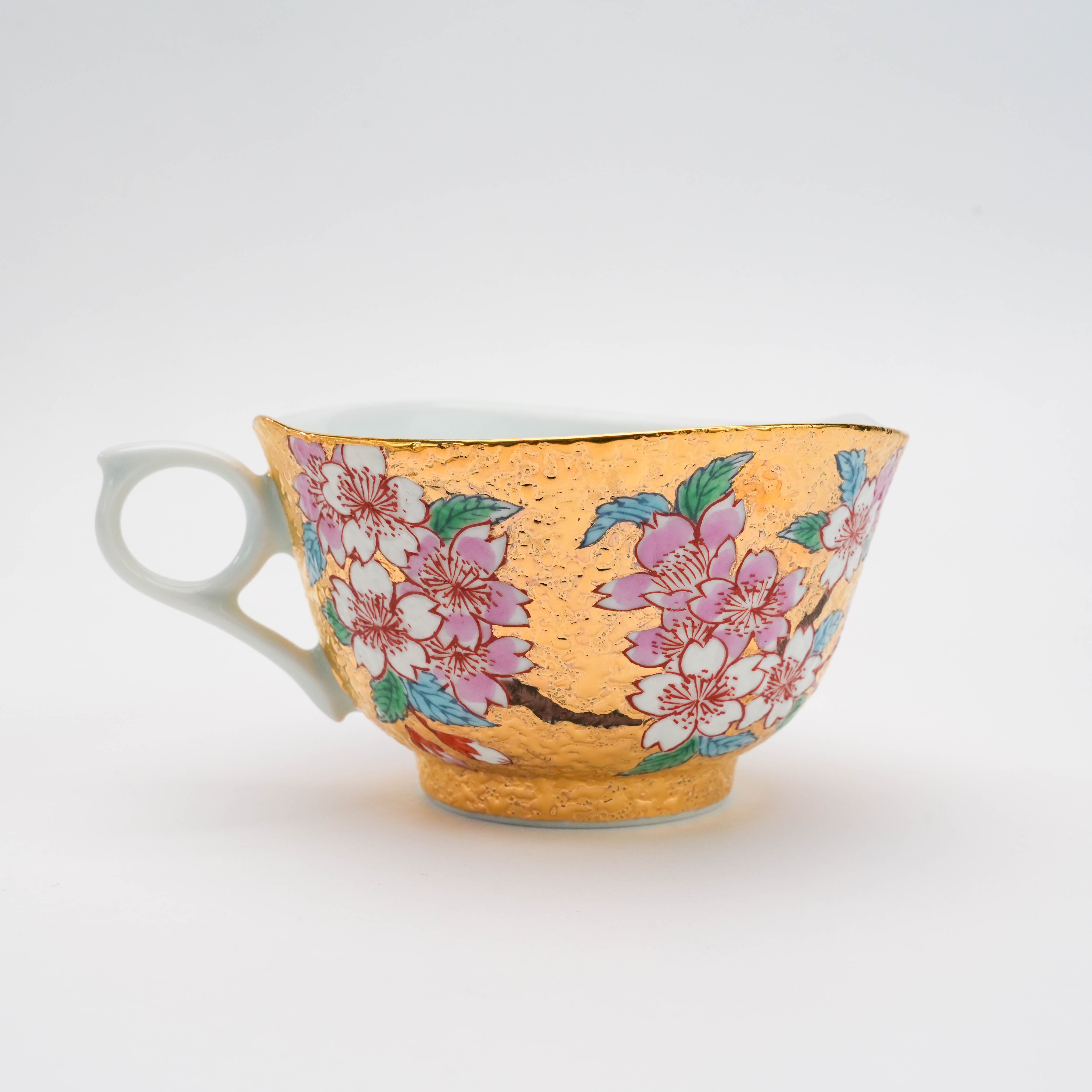 Angled view of the Arita Ware Gold Sakura Cup. Features a unique handle and vibrant sakura motif on shimmering gold leaf.