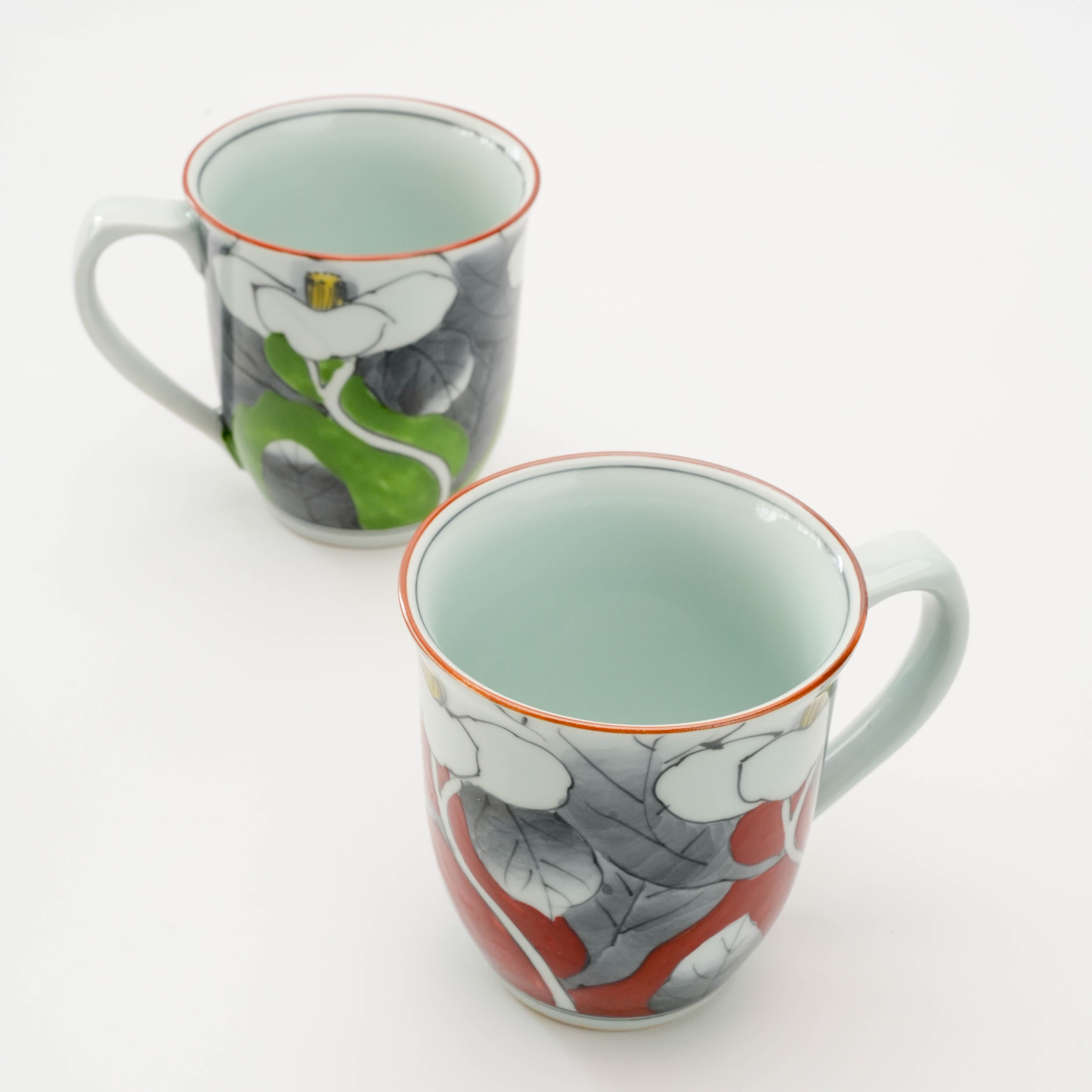 Top view of Arita Ware Sometsuke camellia mugs in red and green, showcasing intricate Japanese floral artistry and fine ceramic craftsmanship.