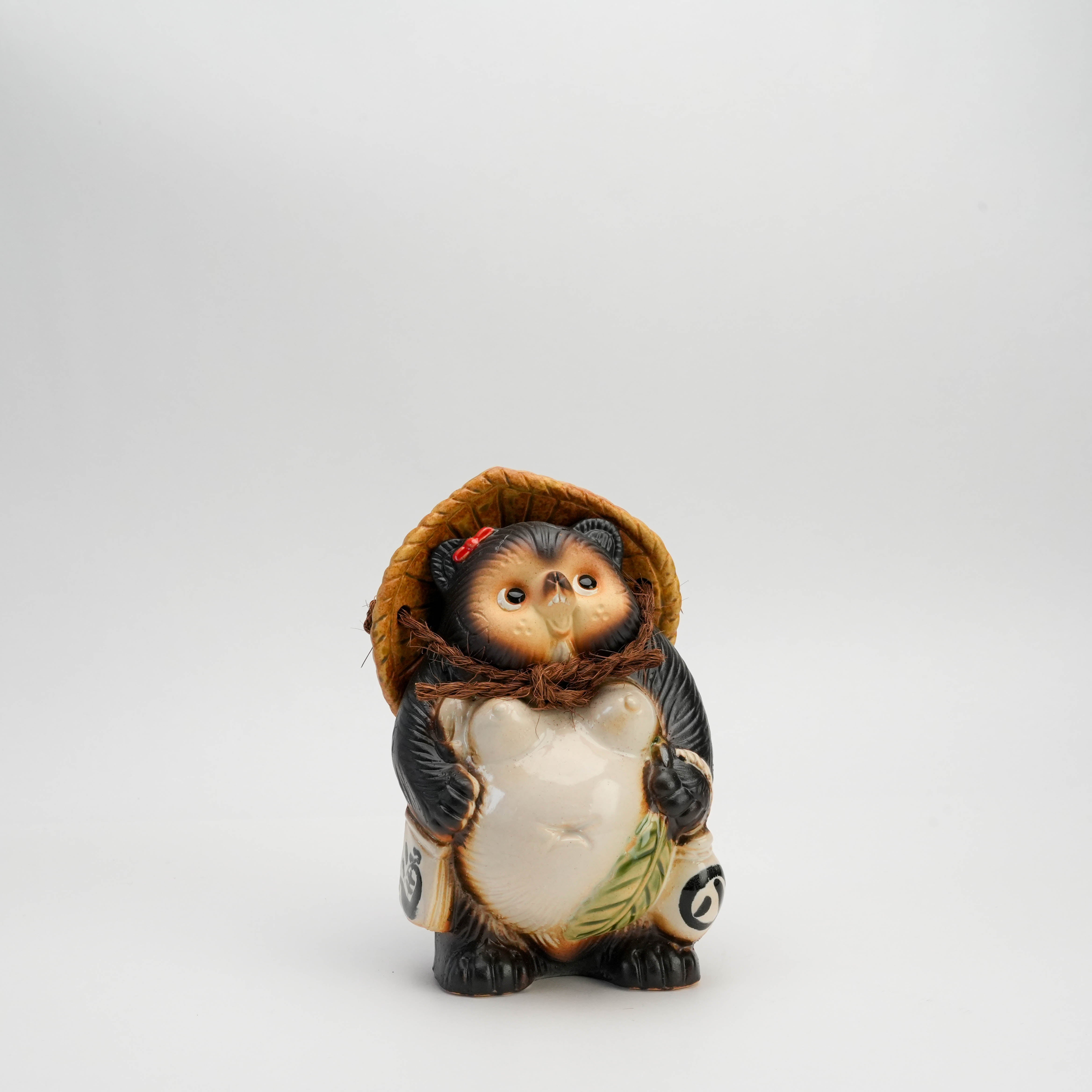 Shigaraki Ware Tanuki Ornament featuring a female raccoon dog with a twisted pose, straw hat, and sake bottle. Handmade good fortune charm figurine.