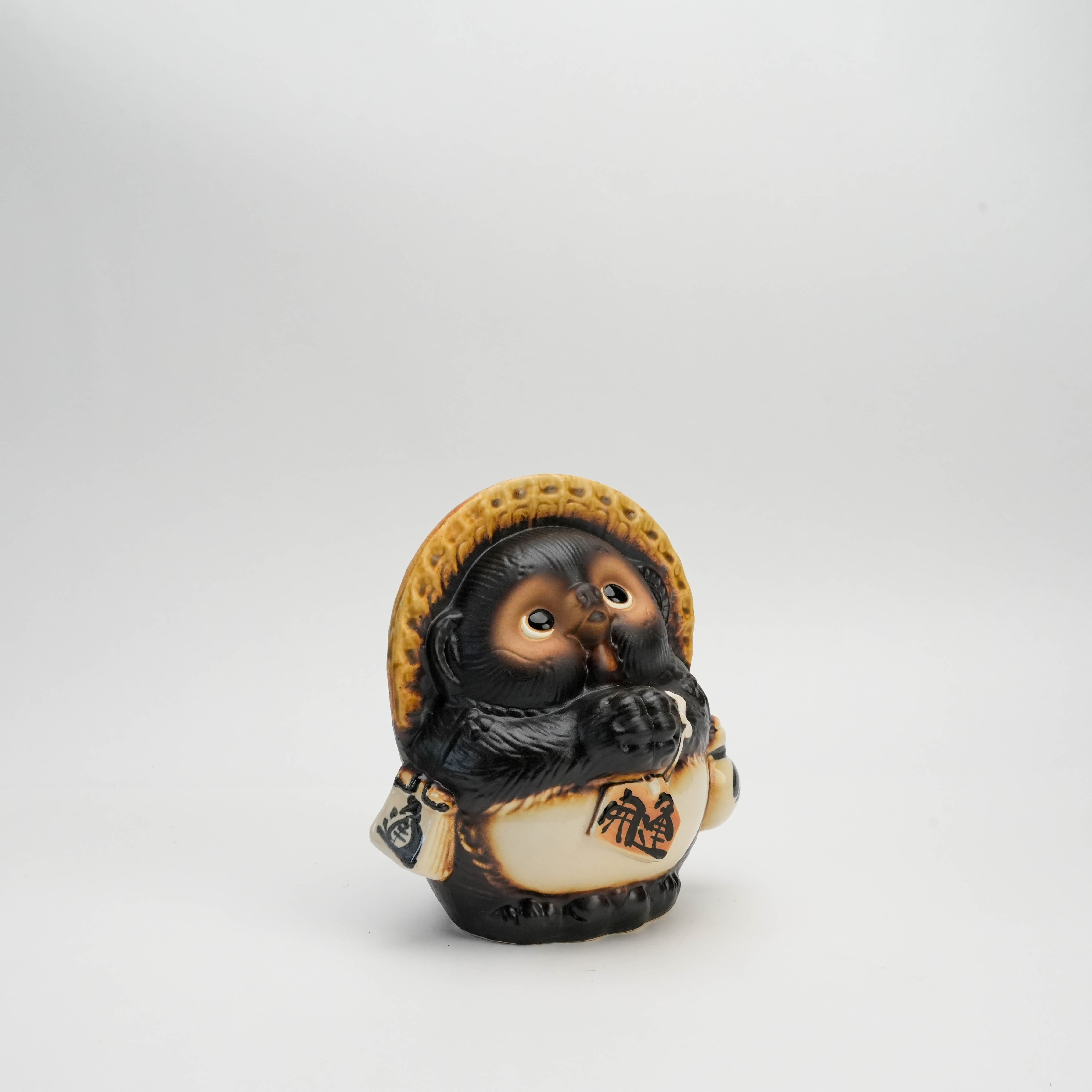 Side view of Shigaraki Ware Tanuki figurine holding a sake bottle and promissory note, ideal for home decor and attracting luck.