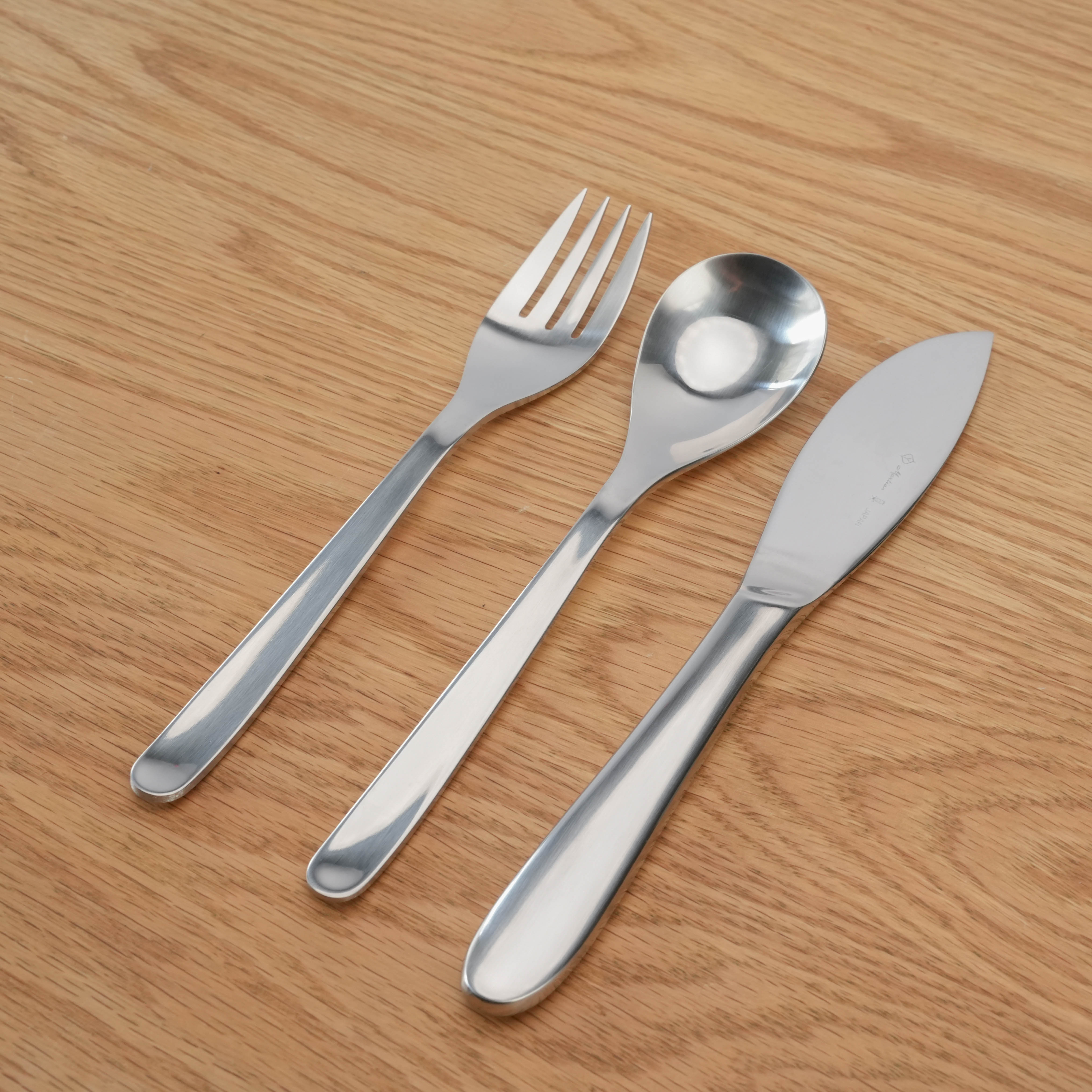Sori Yanagi Stainless Steel Cutlery Set with knife, fork, and spoon on wood surface. Elegant 3-piece dining set for modern kitchens.