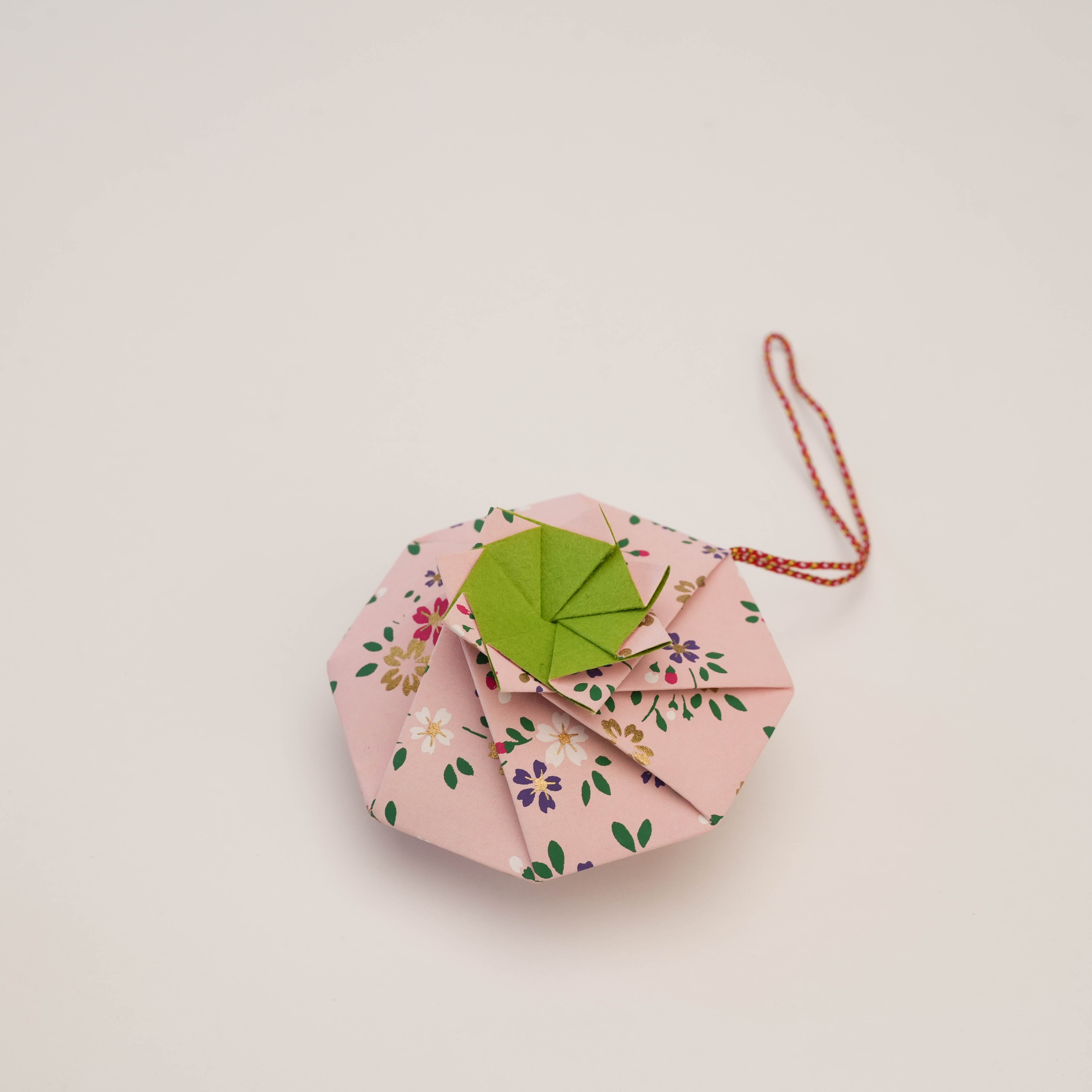 Shoyeido Sachet Flower Wheel in pink origami design with floral print and green center, infused with clove and anise for home fragrance.