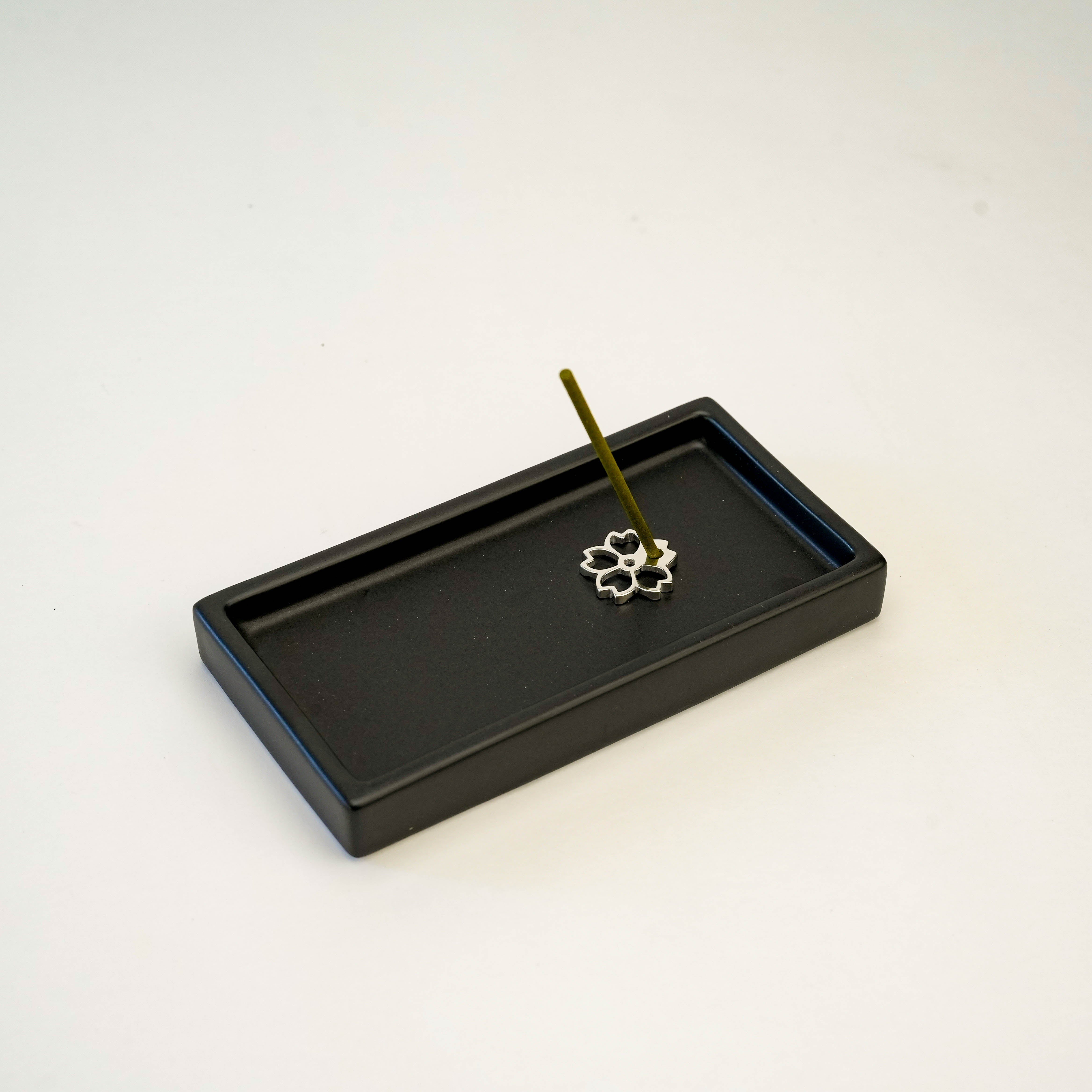 Cherry blossom-shaped Shoyeido Silver Incense Holder in use on a black tray. A stylish incense accessory for modern home fragrance rituals.