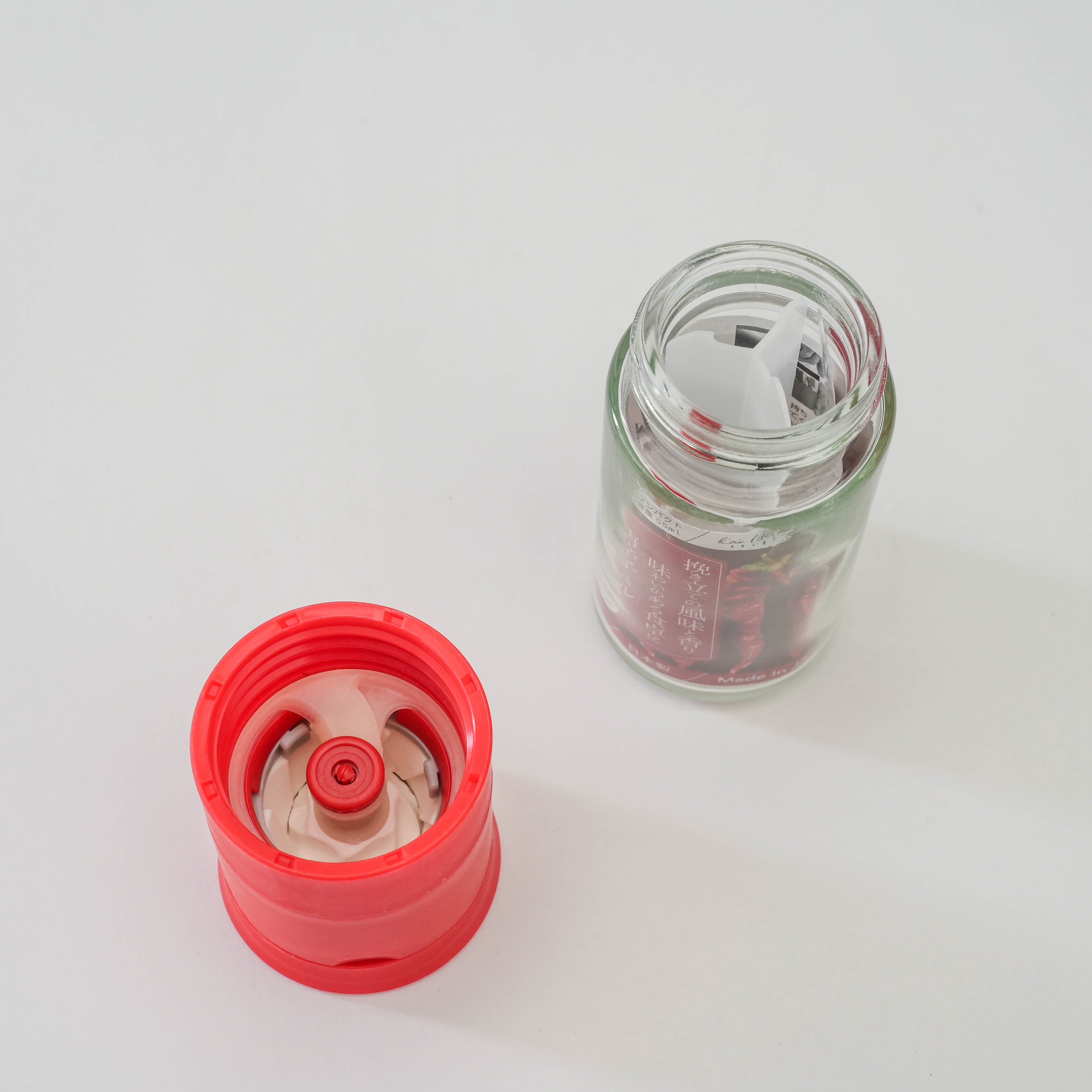 Disassembled Kai Home Ceramic Red Pepper Mill showing rust-resistant ceramic grinding mechanism and refillable glass container.